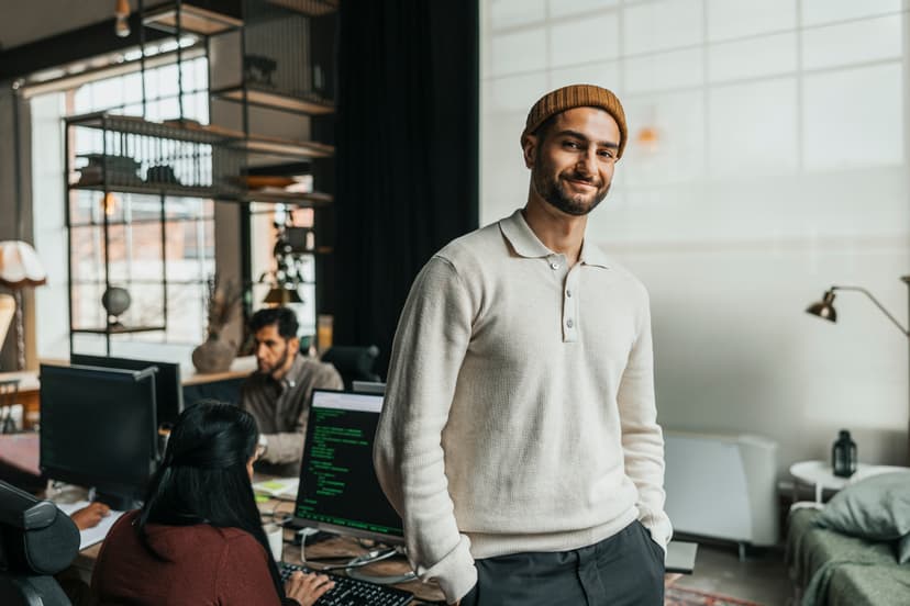 Male worker stands in front of their office environment where computer coding can be seen on a scene behind them