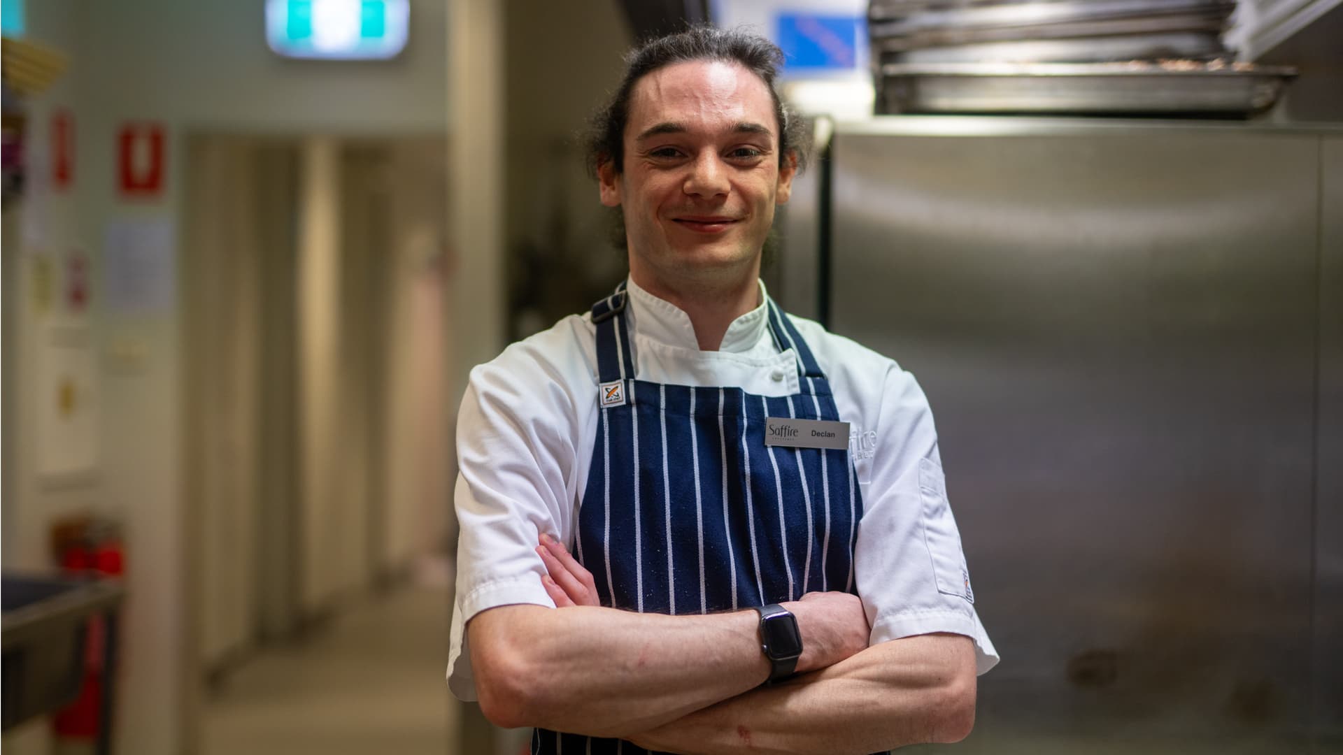 Declan wearing his chef uniform and apron in the Saffire Freycinet kitchen after returning to the career he loves with support from APM