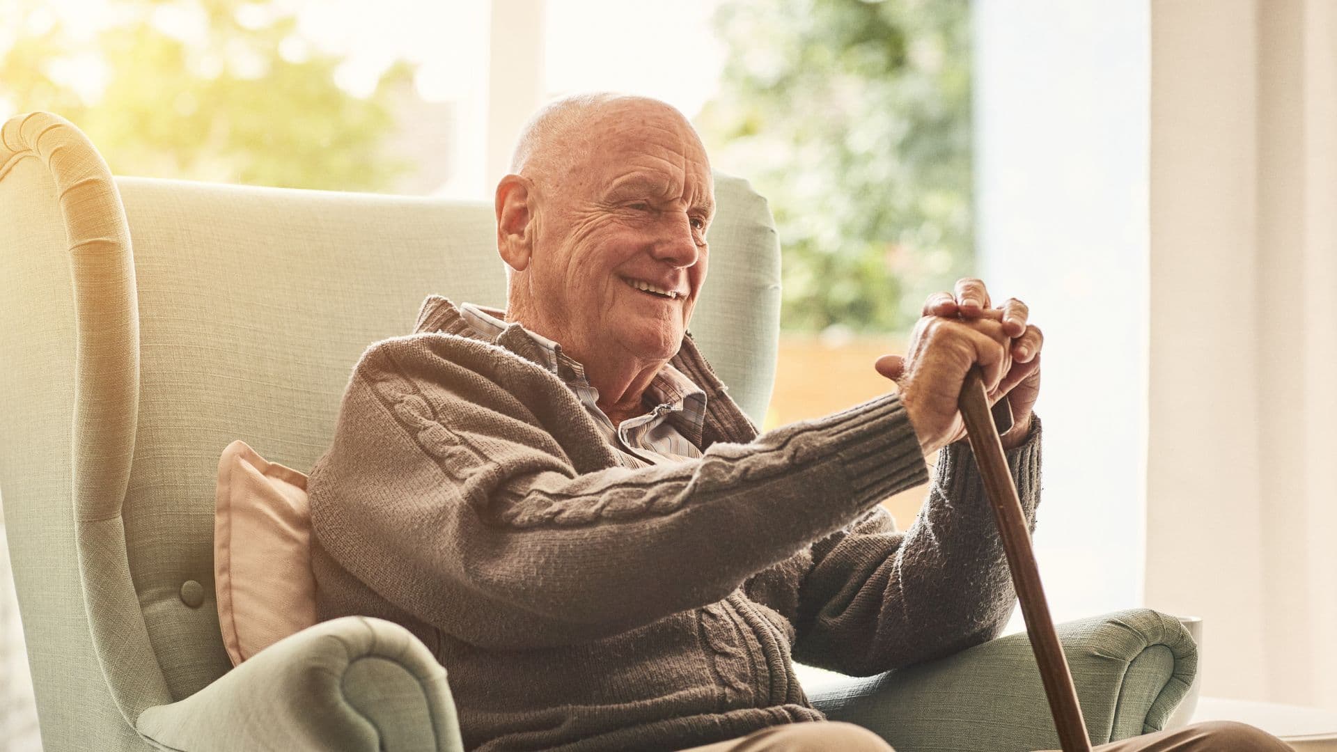Older person seated in a comfortable chair holding a walking aid in a home environment, reflecting mobility and support needs considered in aged care assessments.