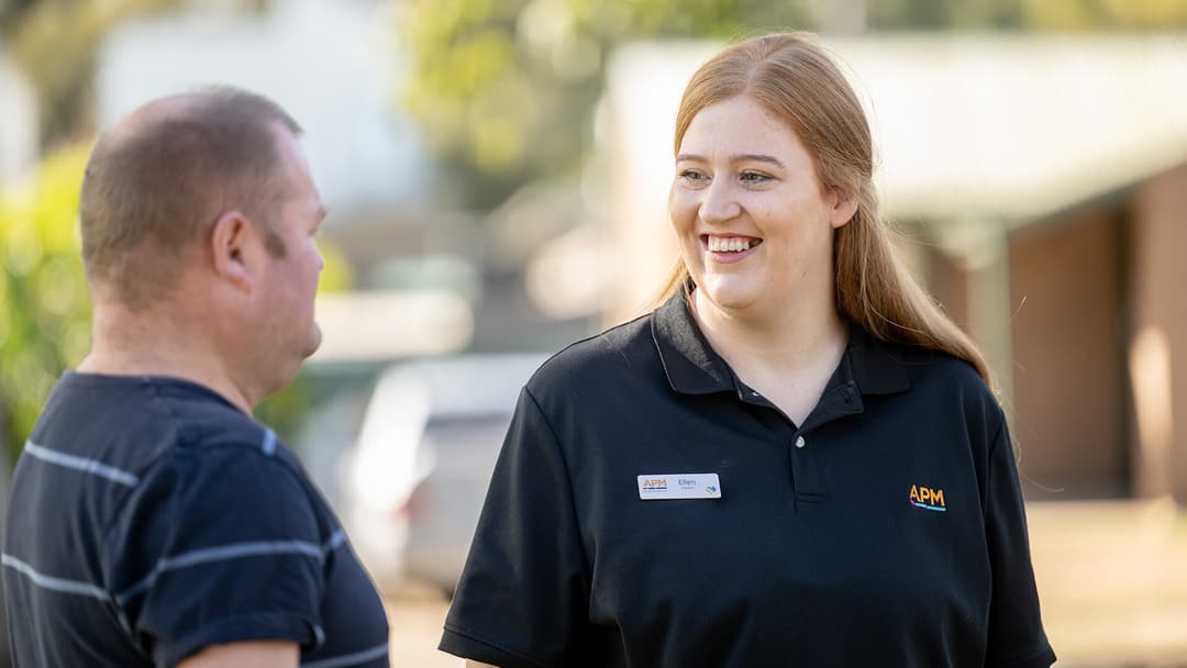 An APM employee in a black polo smiles in conversation with an IEA participant