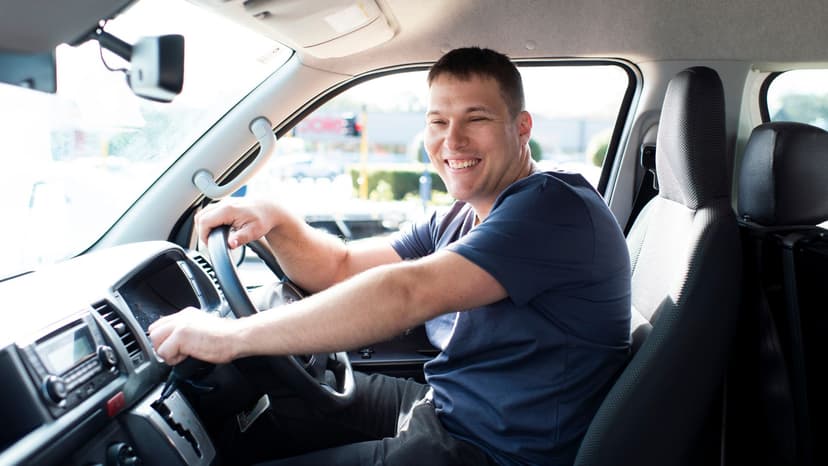 Man smiles in blue shirt behind the wheel of work van