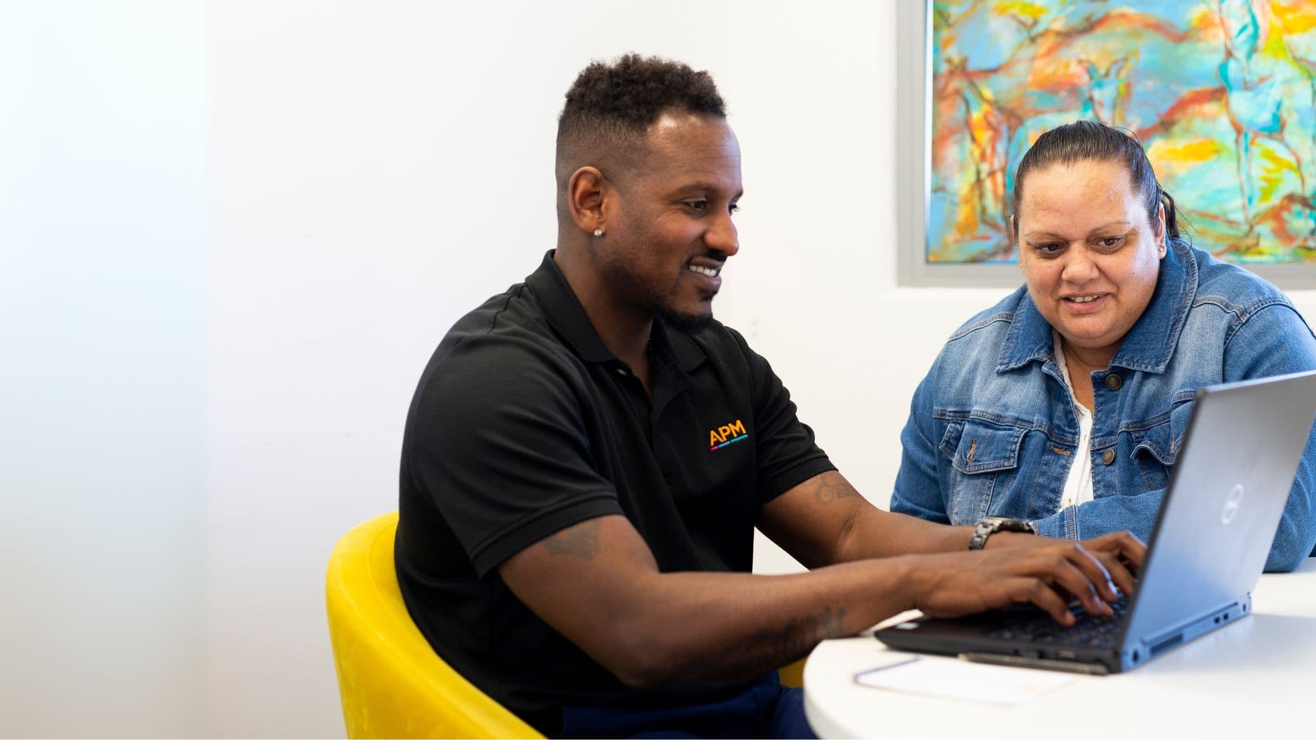 APM consultant Austin sits in an office with a laptop supporting Workforce Australia participant Mel with her employment program.
