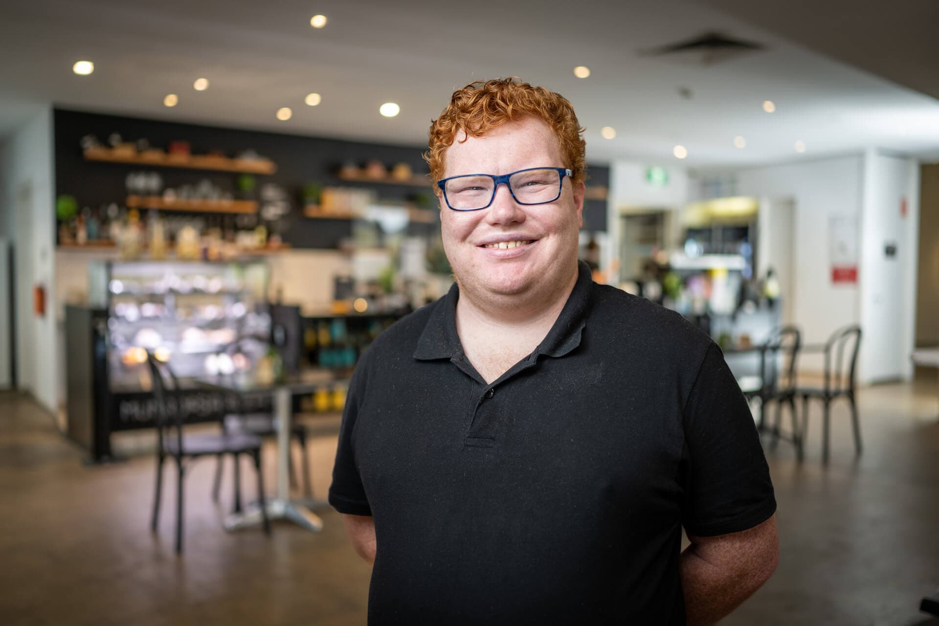 DES participant Andrew smiling after finding a job in the cafe behind him