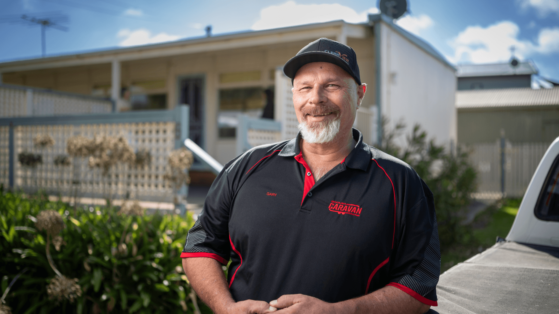 Man smiling leaning on site of UTE in black cap and polo