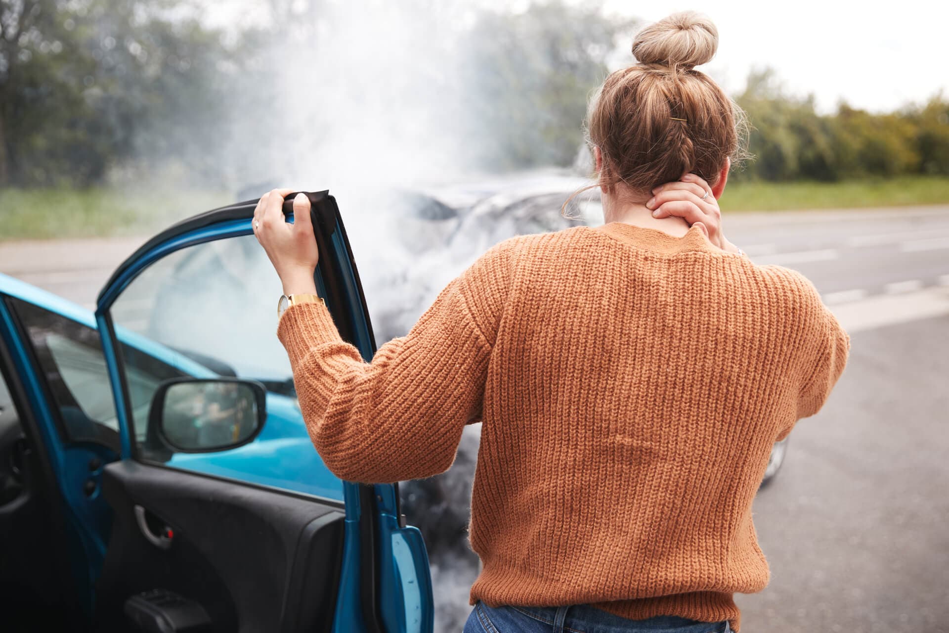 Female driver gets out of their car after an accident holding their neck