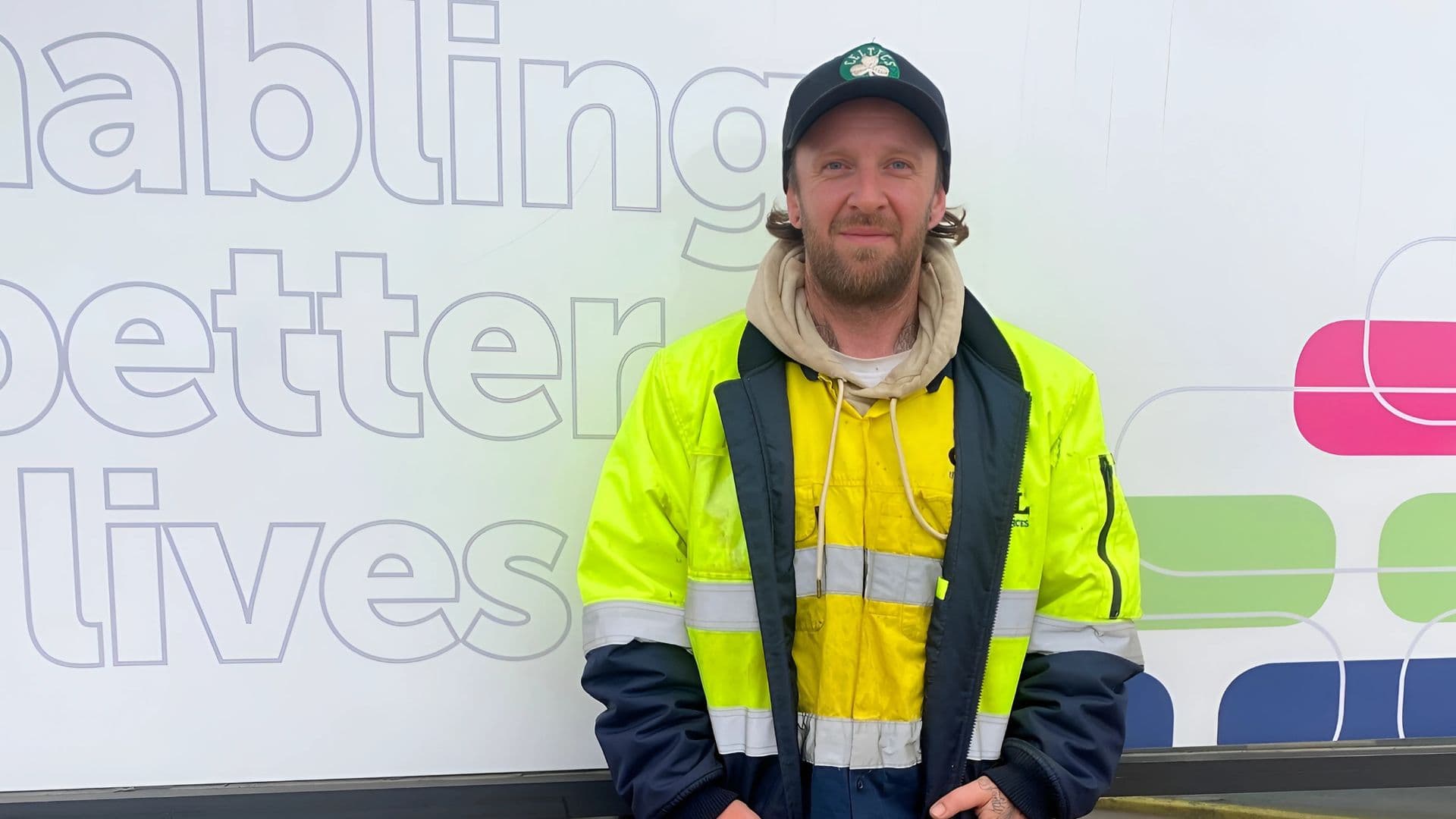 Myran a DES participant stands outside an APM branch in a high-vis jacket and green cap