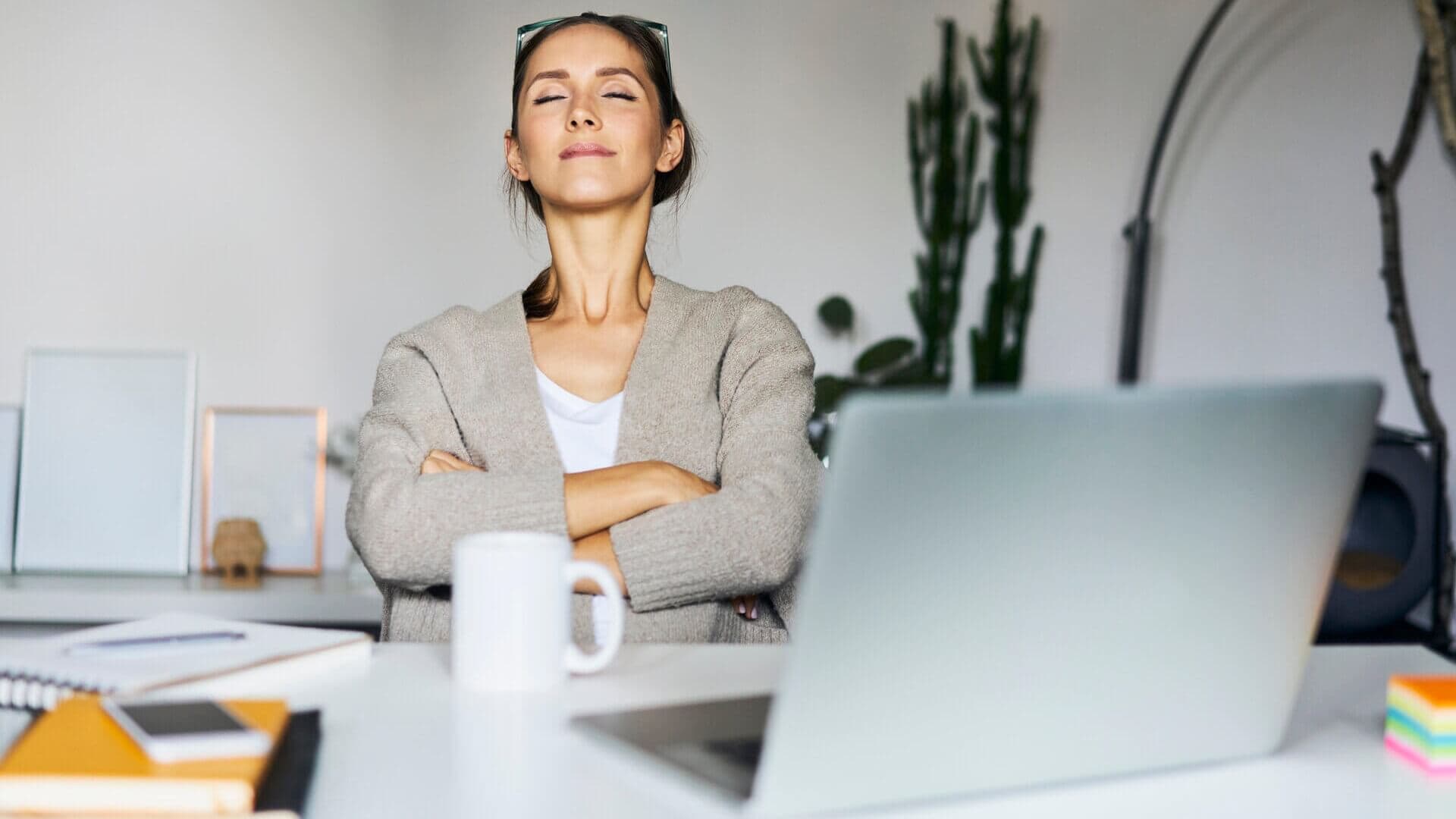 A female office worker relaxing at her desk with eyes closed and arms crossed