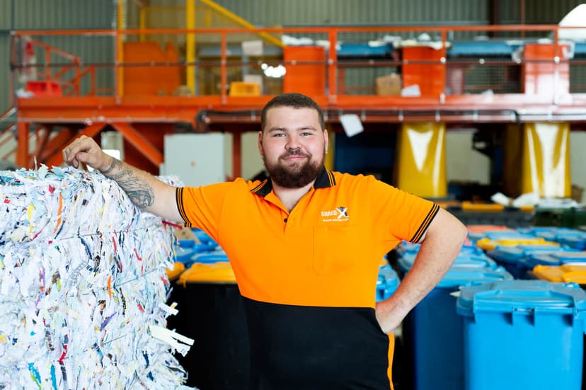 Participant Jarryd smiles standing next to a stack of shredded paper