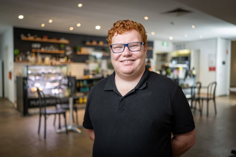 Andrew a DES participant smiles in his cafe workplace in a black polo