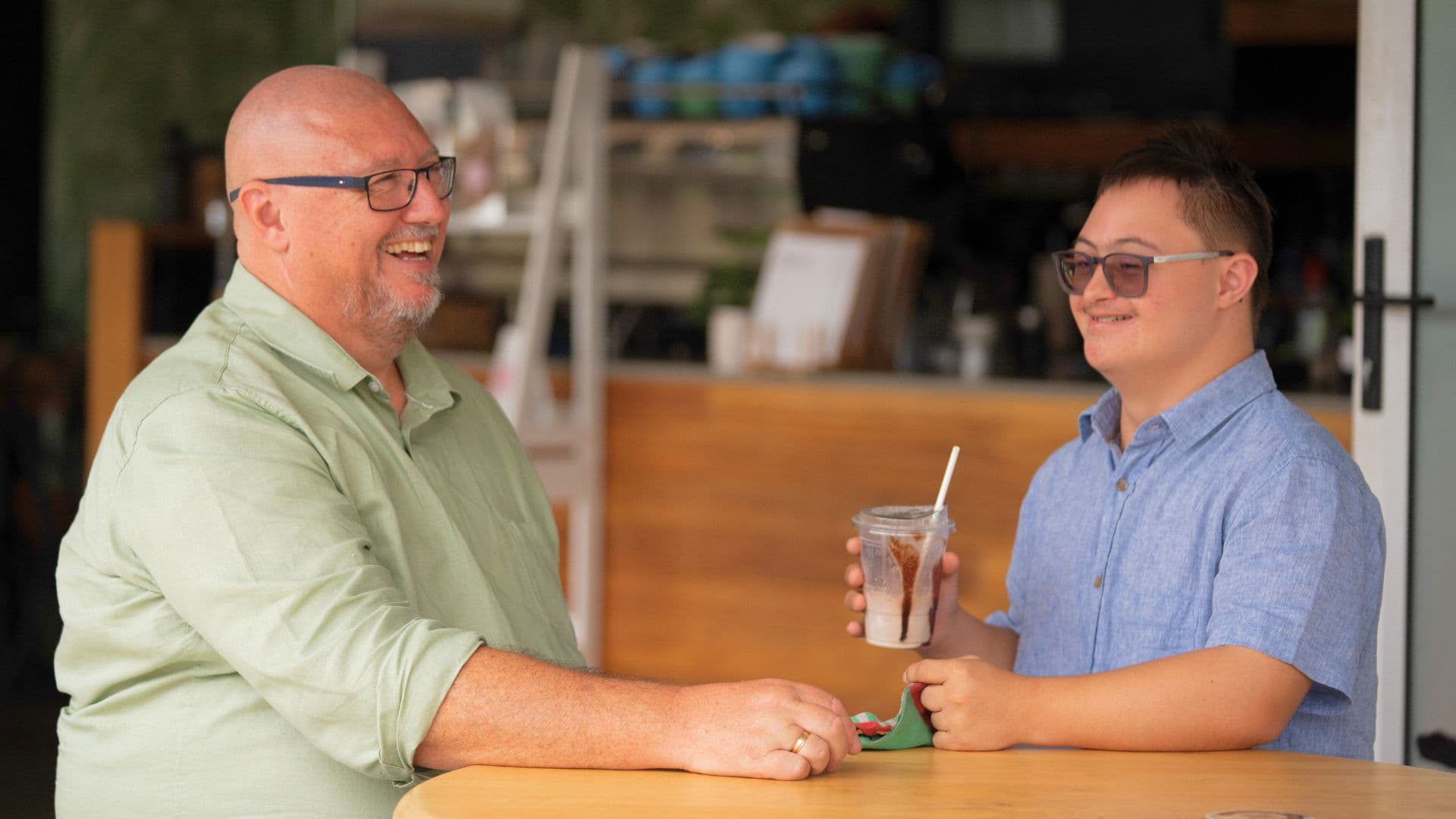 Liam and his dad Casey sit at a café table smiling