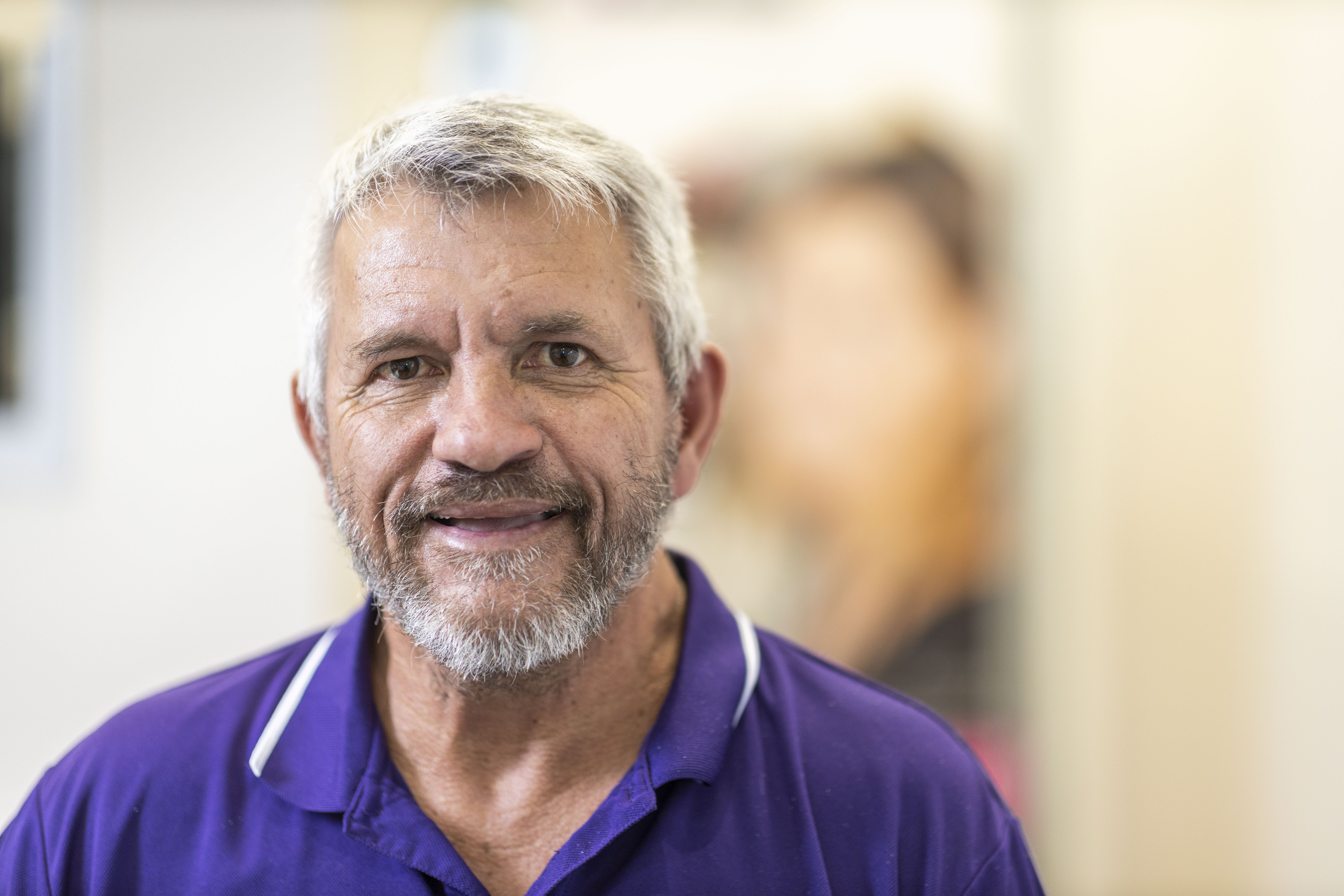 Jeff smiling in his purple uniform top leaning on an office wall