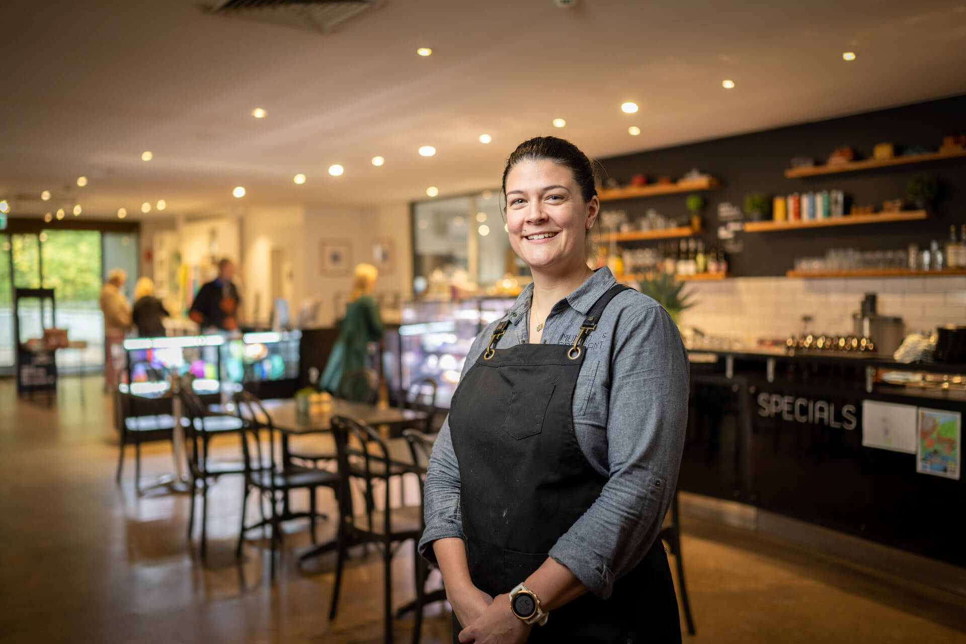 Cafe owner stood in black apron smiling with shop in background