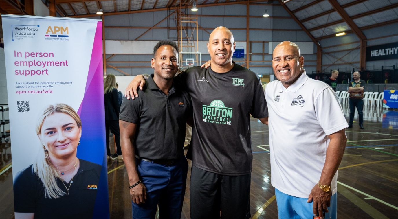 Three men from the APM and BBF partnership smile together on basketball court