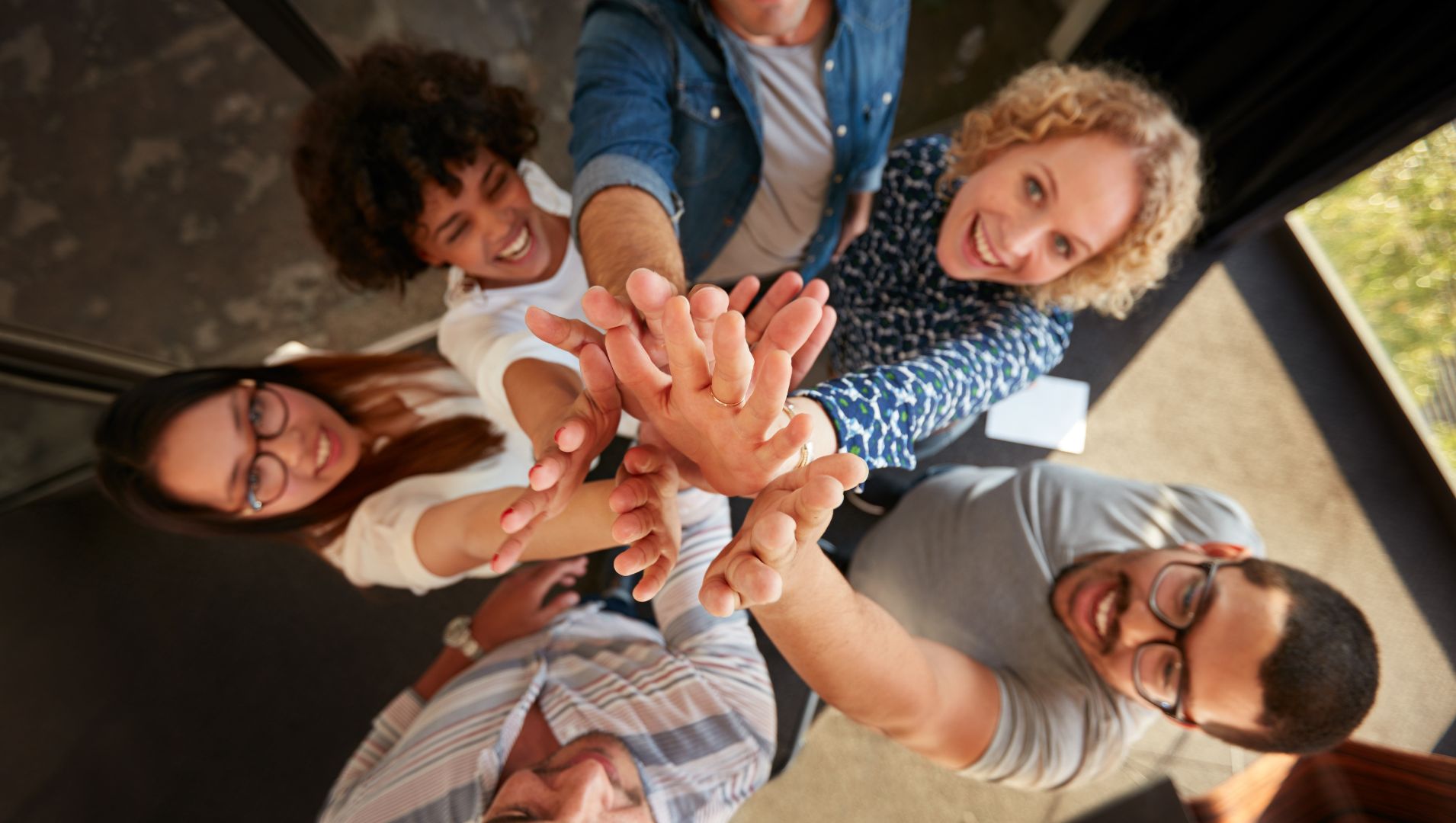 A resilient team work together and put their hands in a circle looking up at the camera.