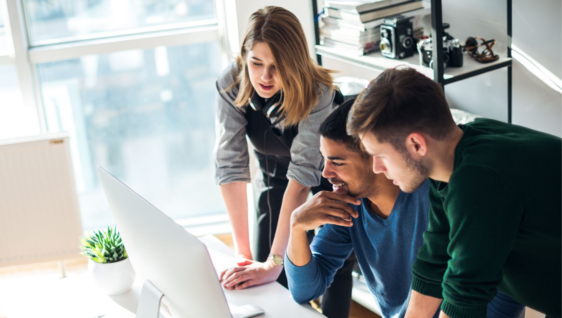 Three colleagues work together at a computer screen to discuss a stressful project