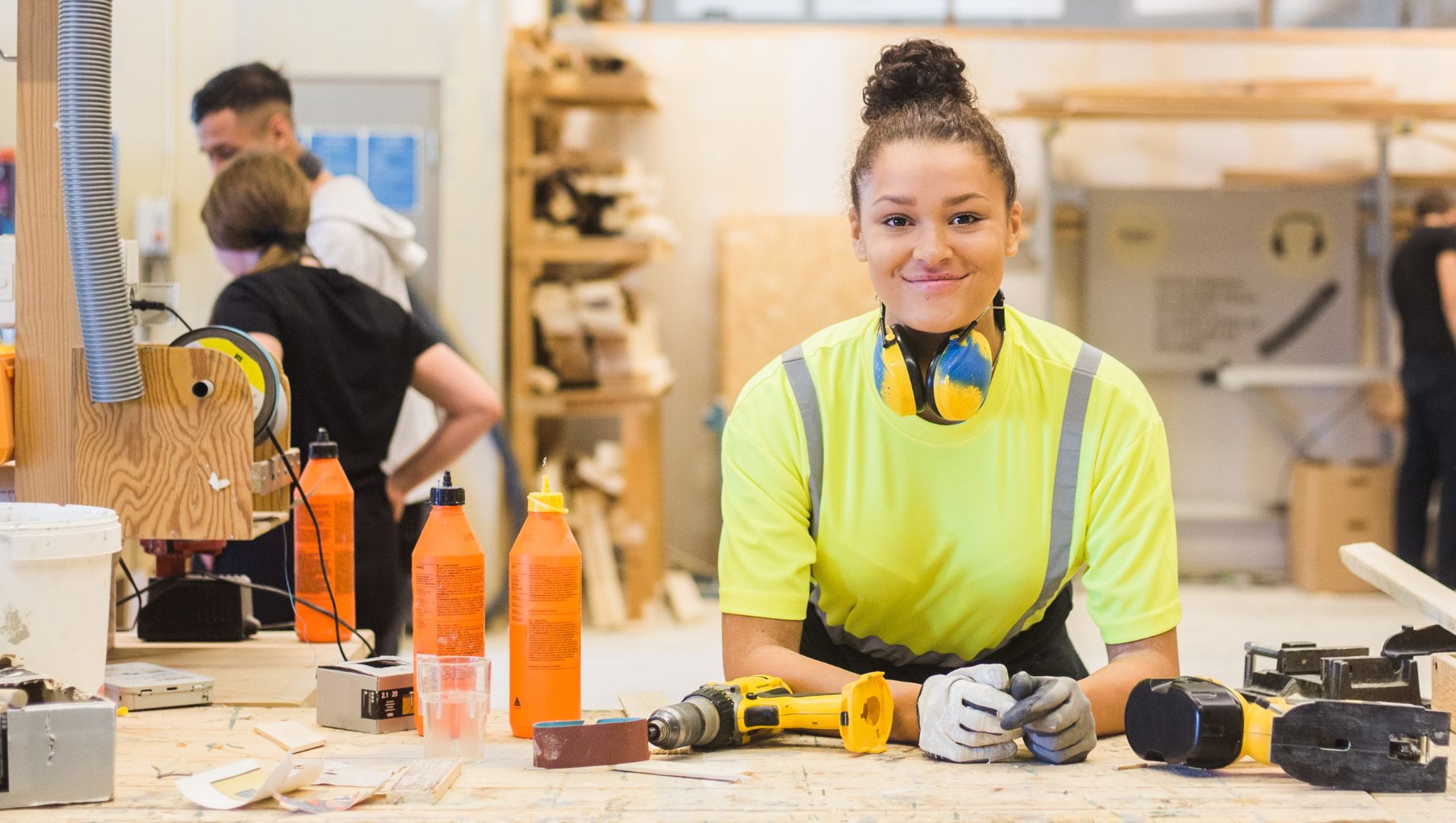 Young woman apprentice smiles at a work bench 