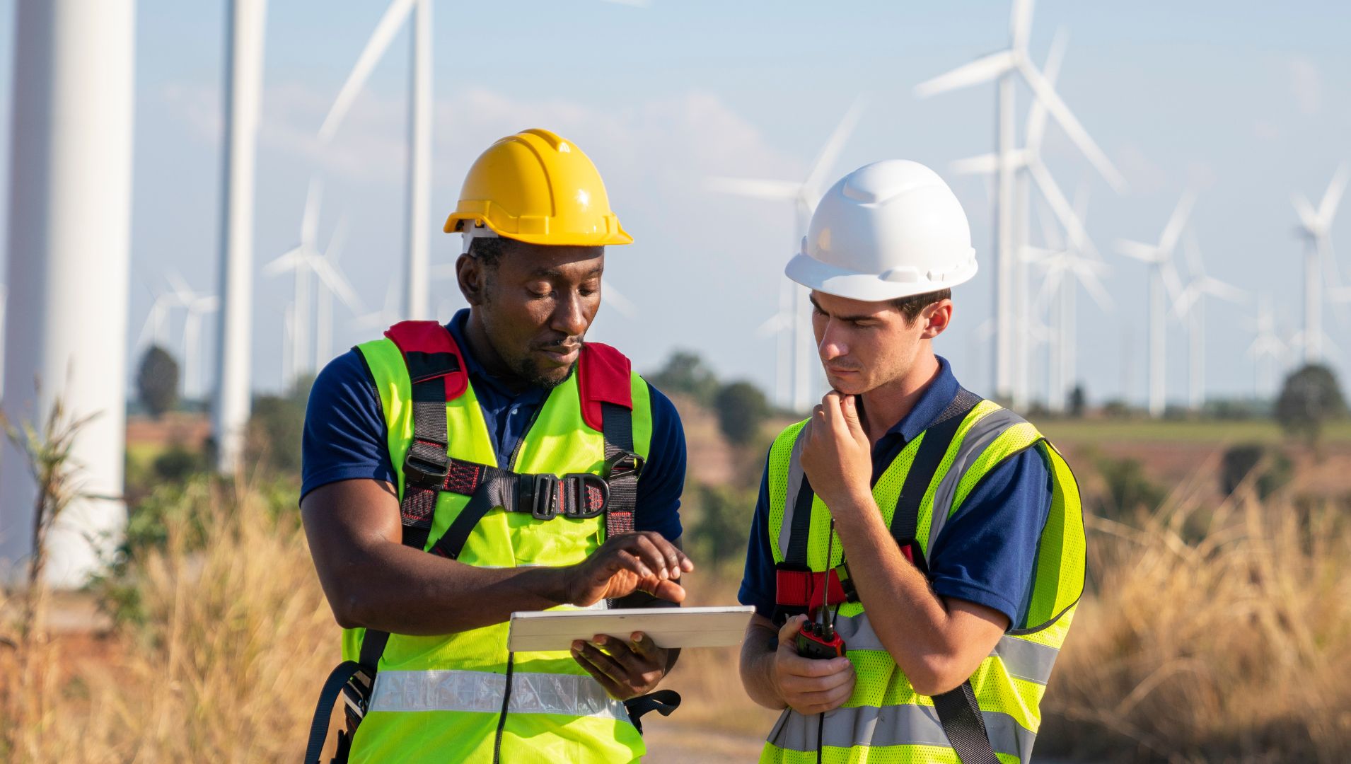 An apprentice and employer look at plans near a field of windfarms