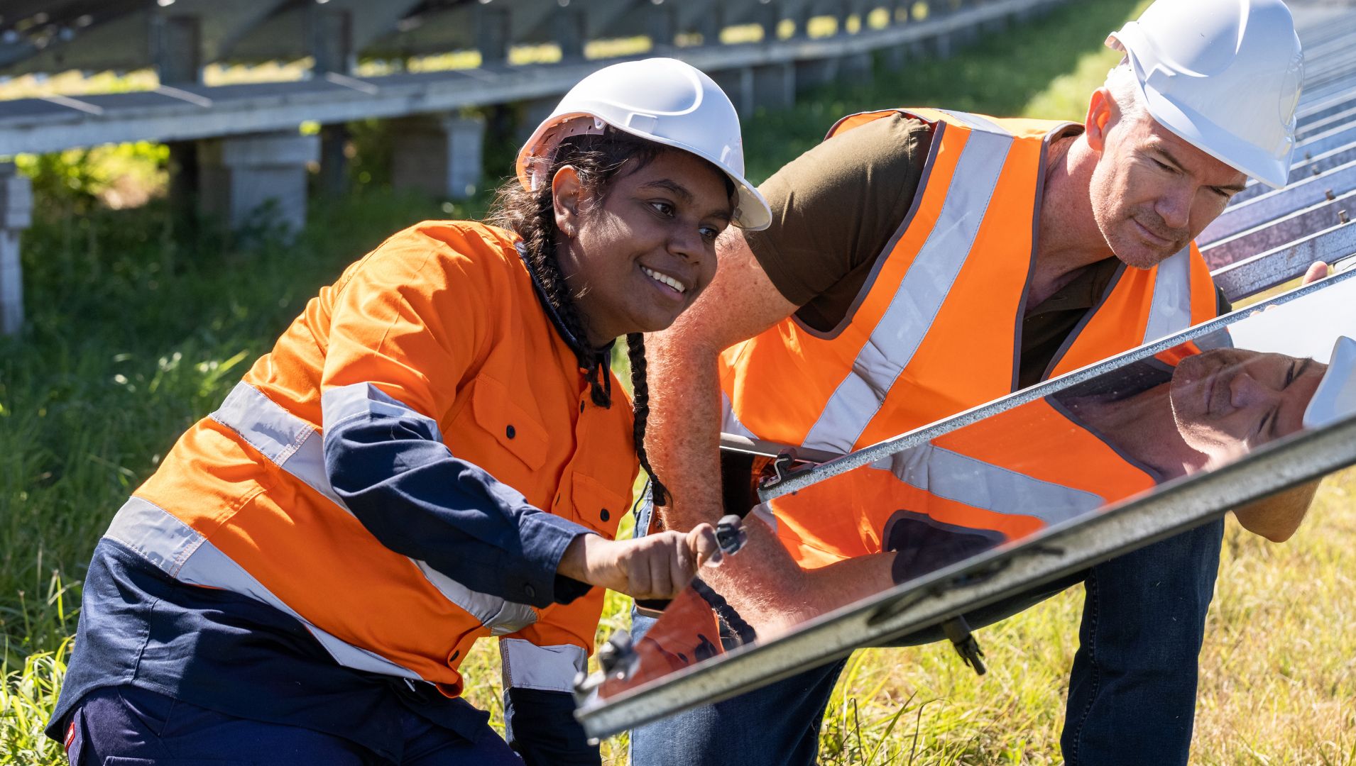 Young female apprentice smiles at camera in front of solar farm