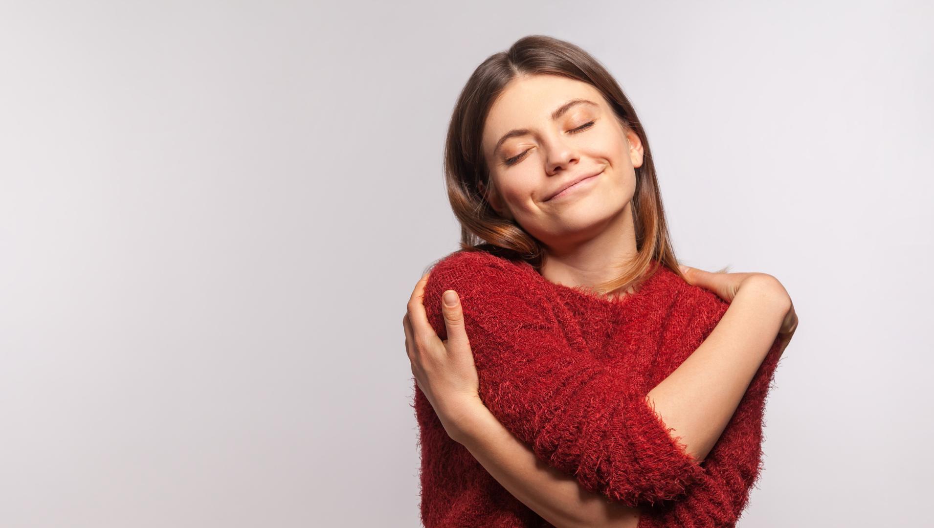 A woman crosses her arms to hug herself and smiles to show she's taking care of her mental health.
