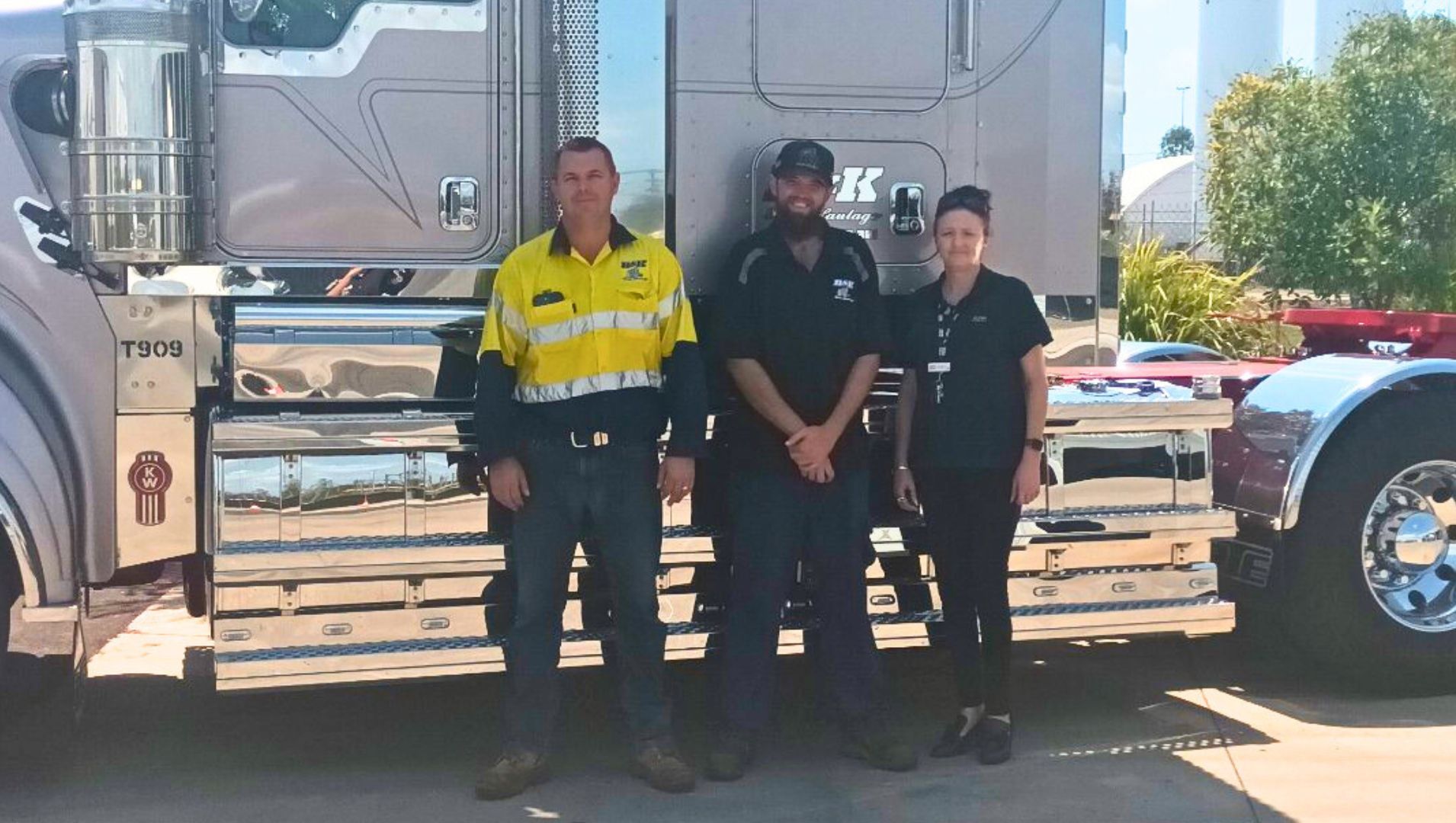 Daniel found a permanent job he loves with support from APM Employment Services. He stands next to a silver truck with employers Ben and Kacey.