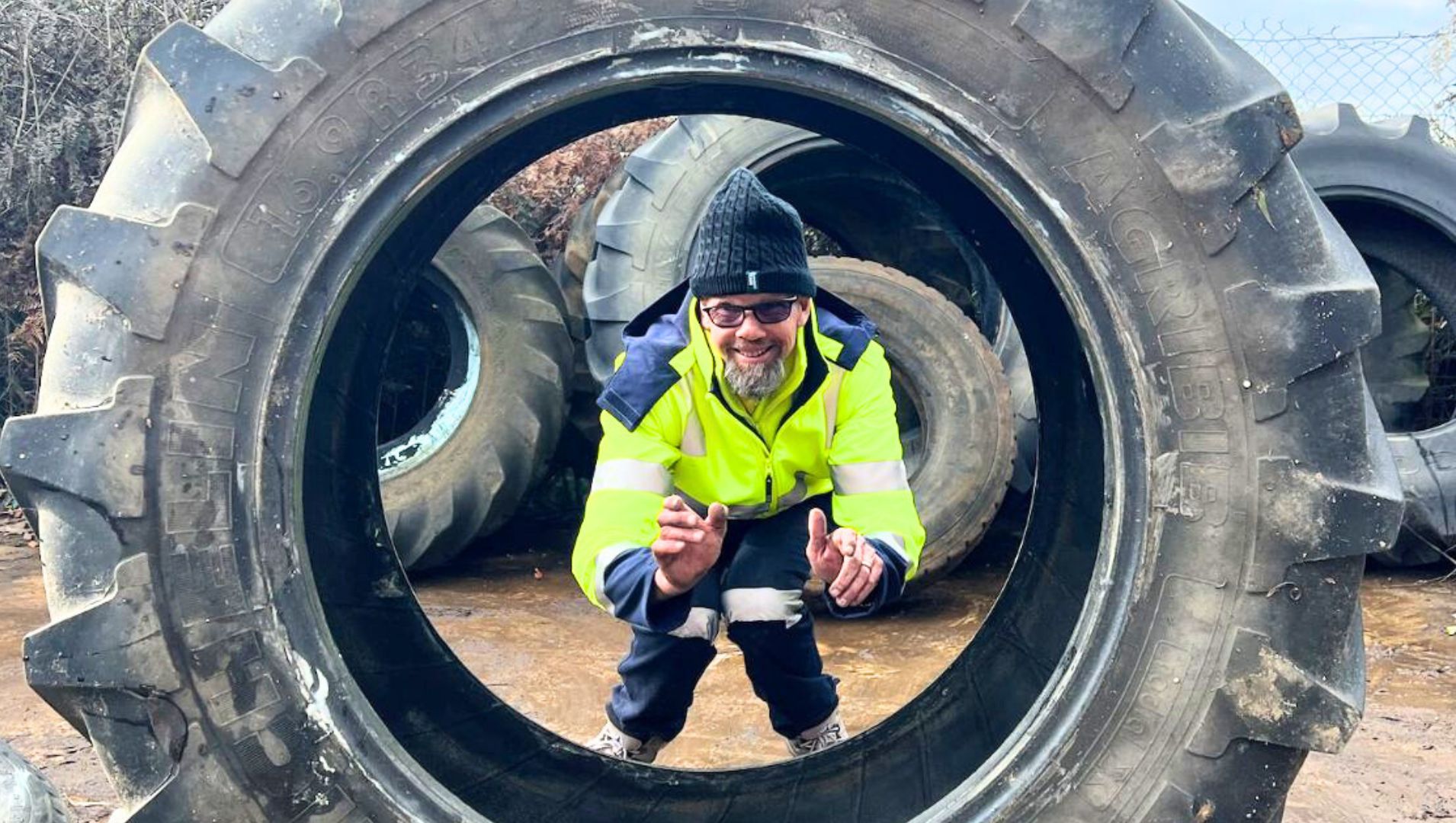 DES participant smiles through a large tyre at his job he found with support from APM Employment Services