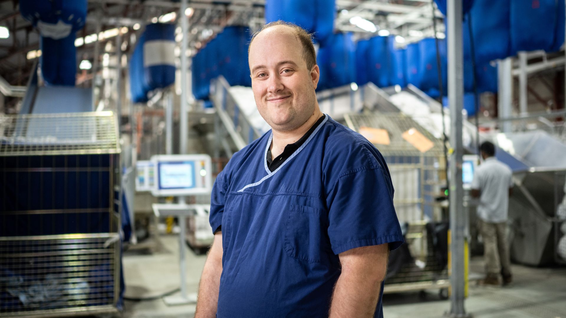 Stephen smiles in a blue work top in a factory