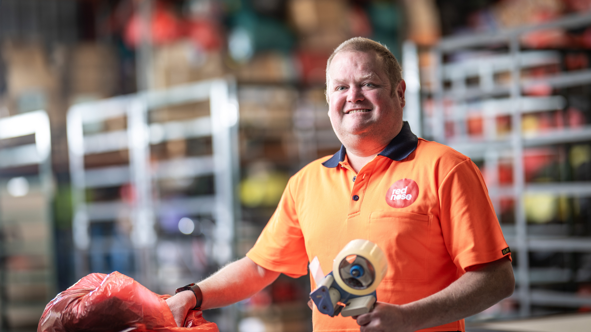 DES participant Eric smiles in an orange top holding a tool in a warehouse