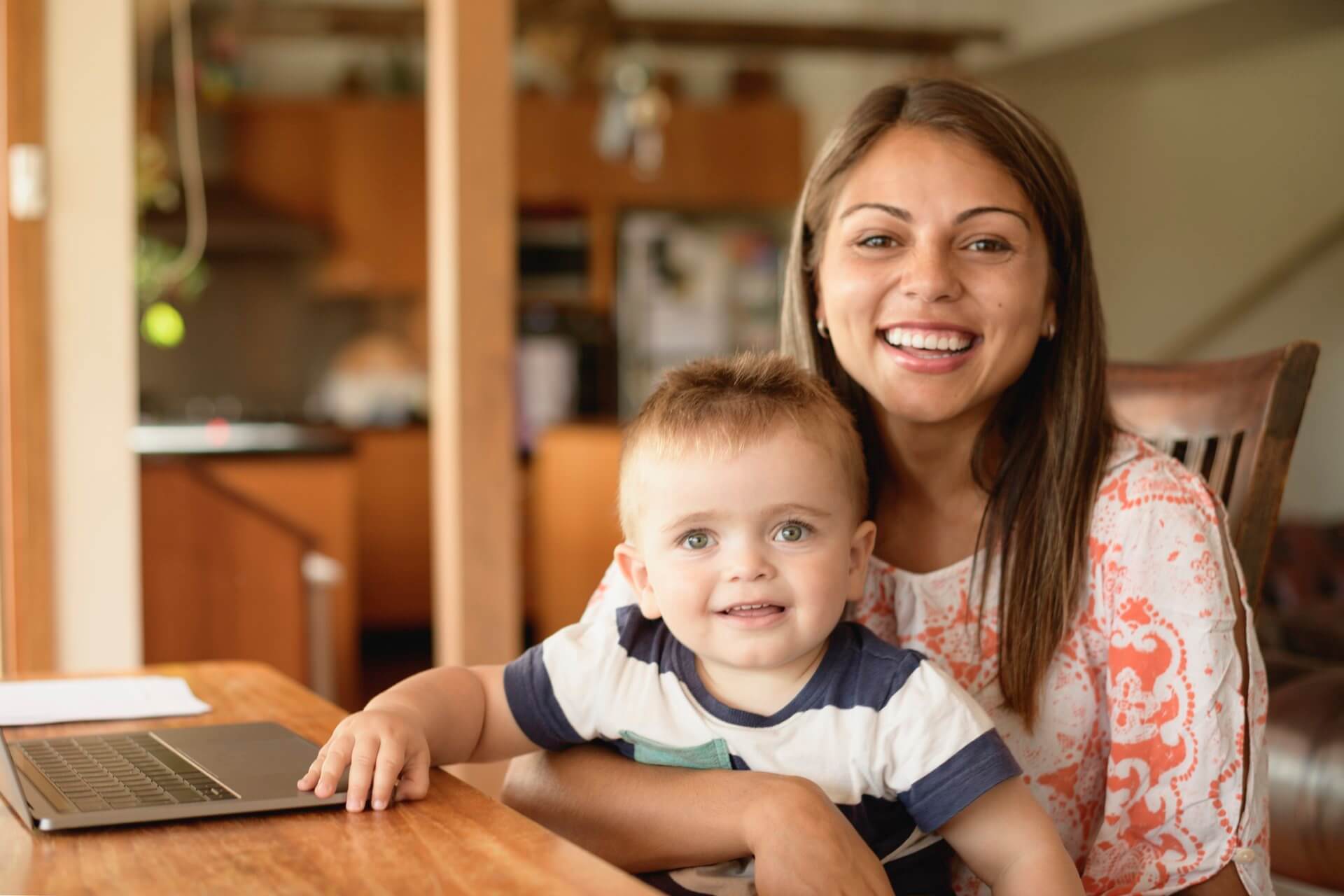 A smiling young mother sitting at a dining table with her toddler
