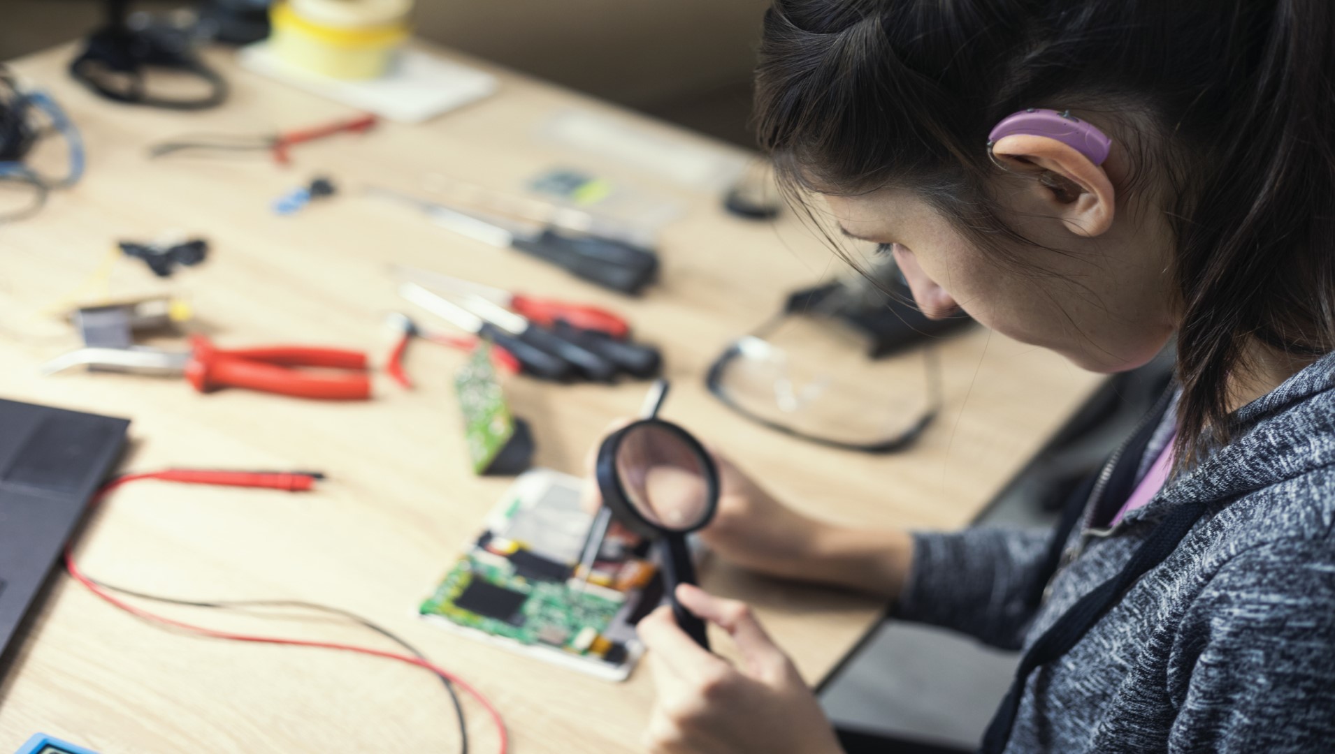 A woman with a hearing impairment working on some electronic repairs at her desk