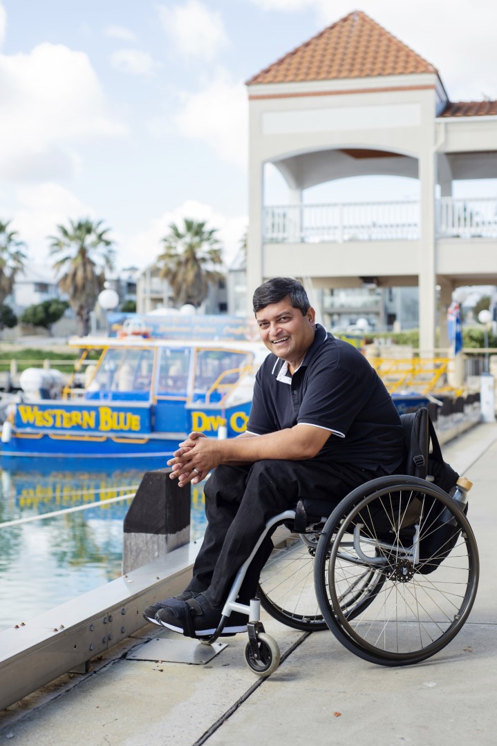 A man in a wheelchair, with a happy expression on his face pictured in front a body of water