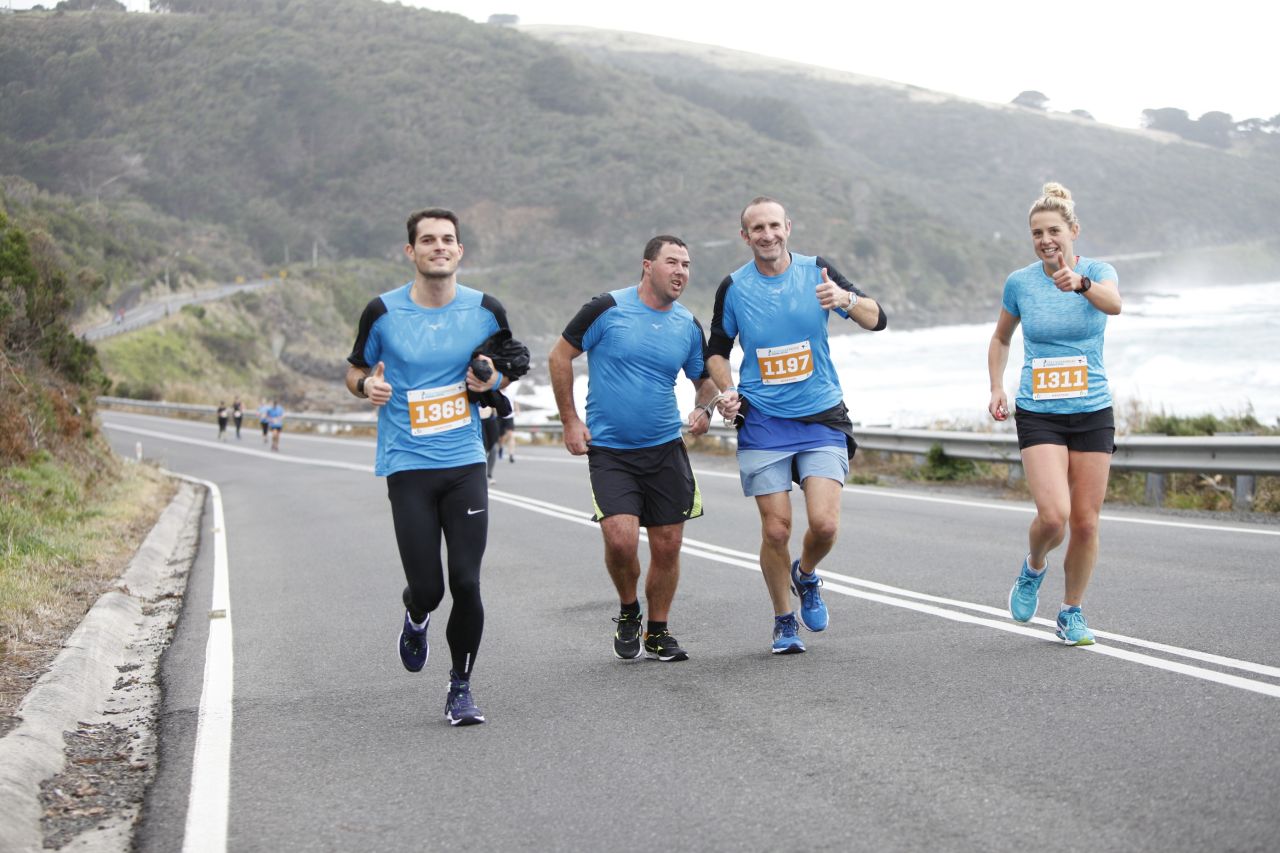 Four people running up a hill smiling to the camera