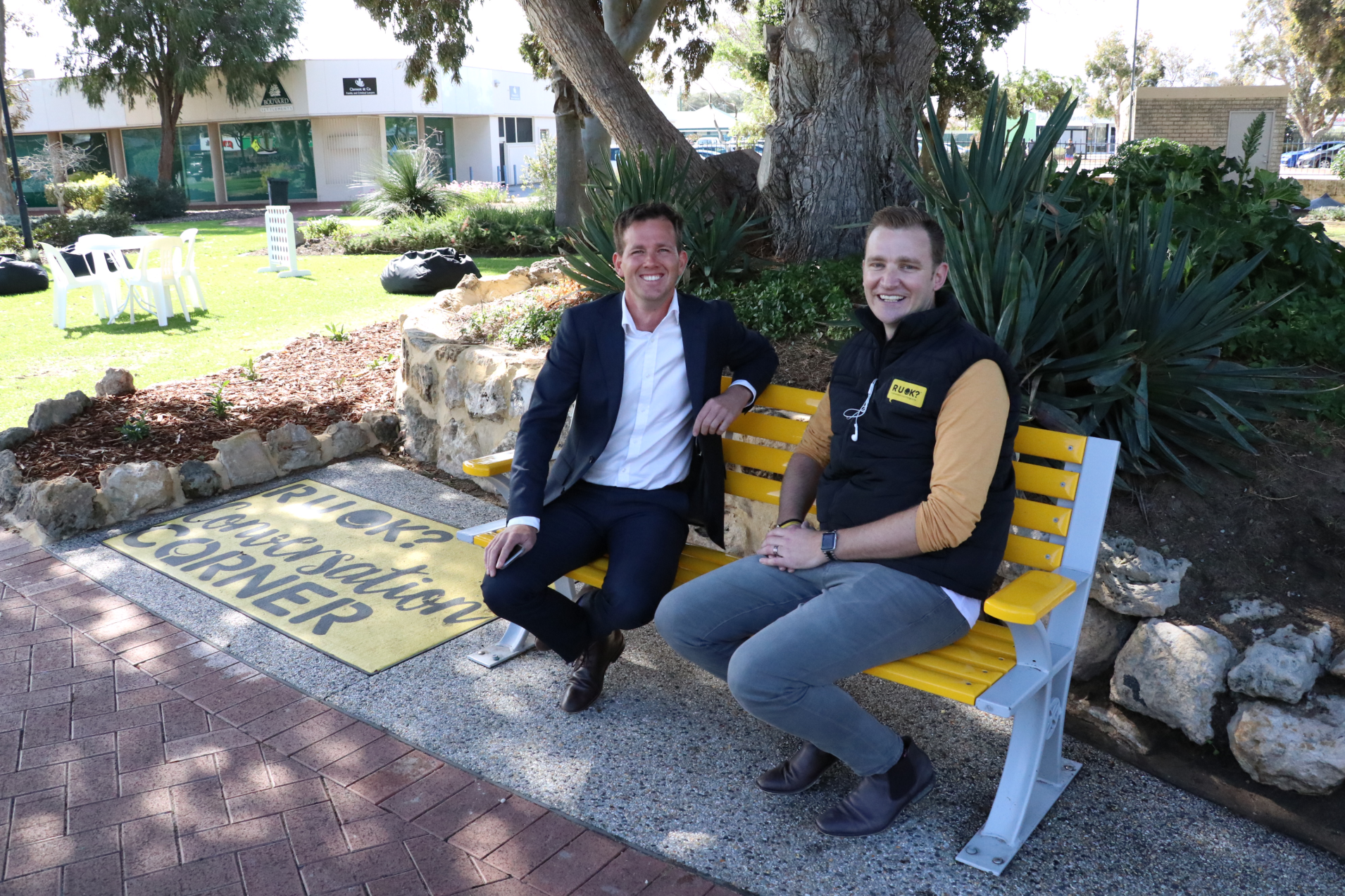 Two men sitting on the yellow bench, smiling up at the camera