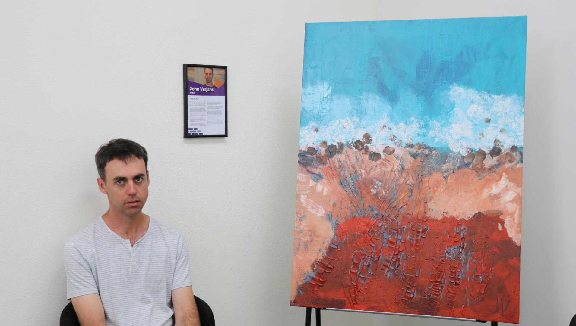 Artist John Verjans is pictured sitting beside his artwork