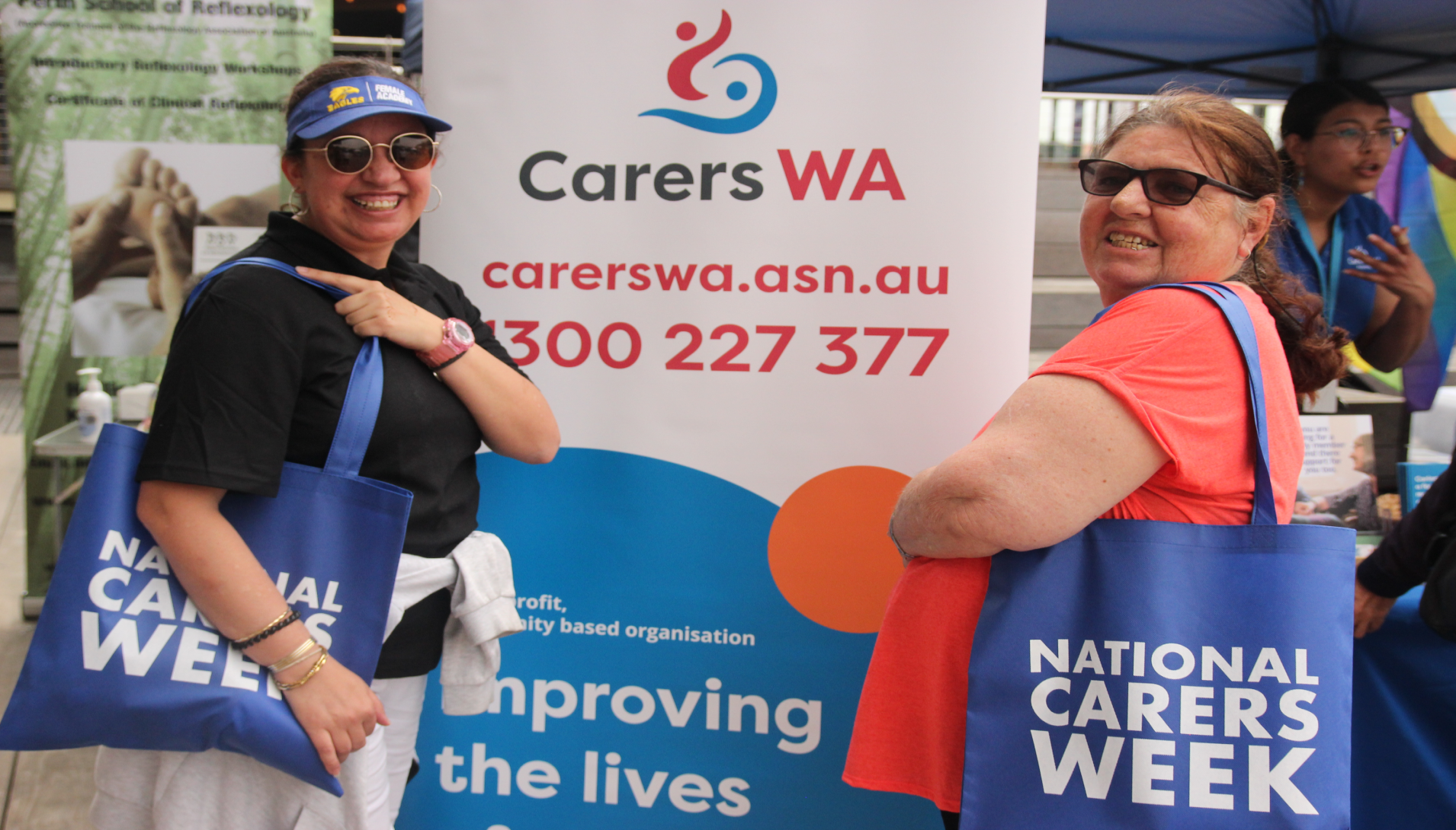 Two women at the Carer's week event standing happily in front of a banner