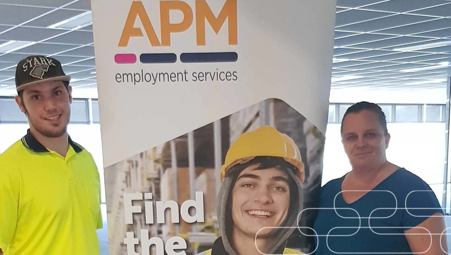 Riley astanding in front of an APM banner in his work uniform smiling