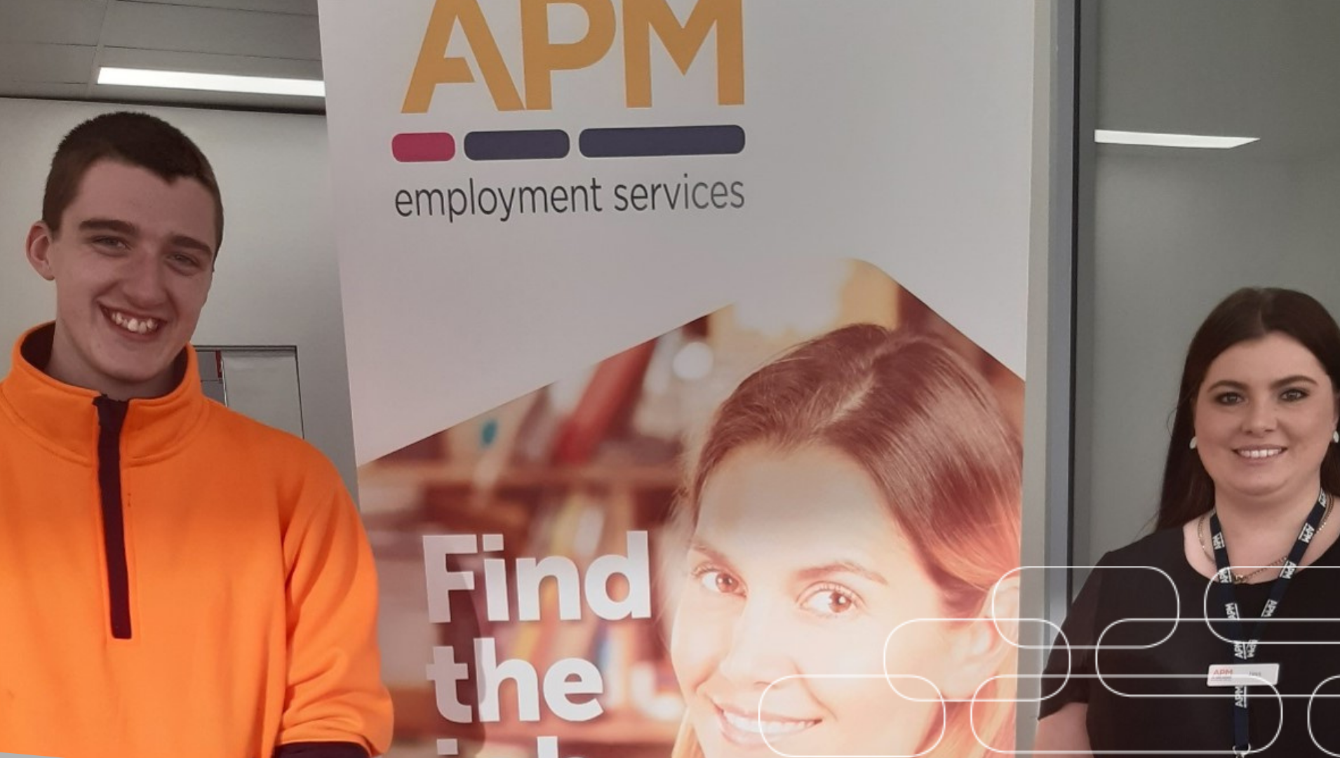 Brandon stand on the left of and APM corporate banner, flanked on the right side is his employment consultant Jess, both smiling
