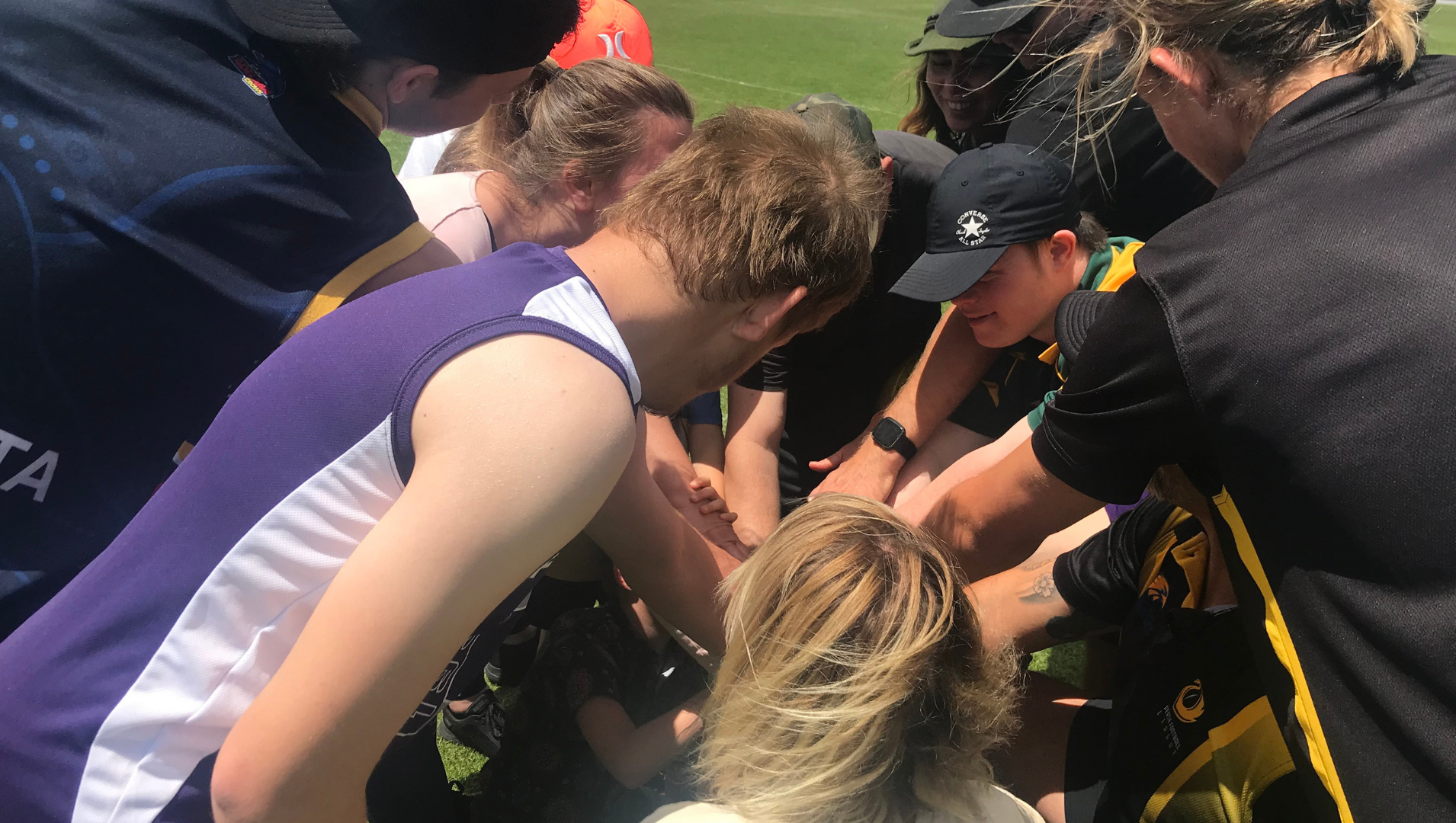A group of participants from the footy open day in a team huddle on the oval