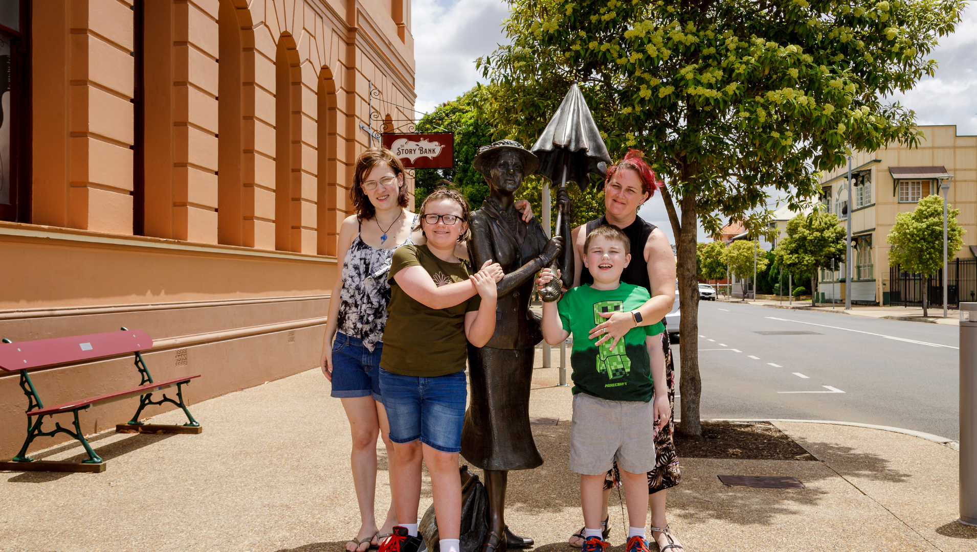A photo of all 4 members of the family, posed around a statue of Mary Poppins