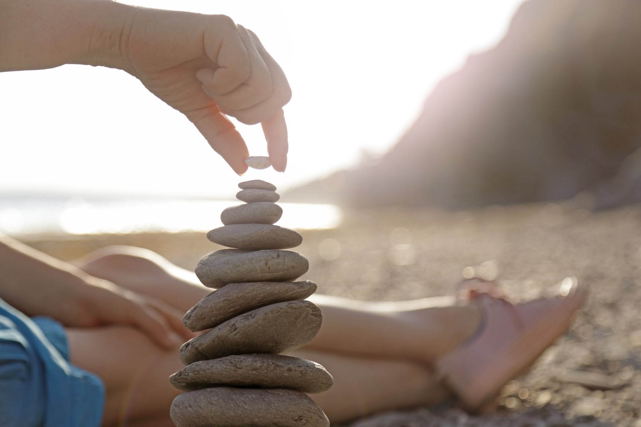 a hand balancing pebbles on a beach