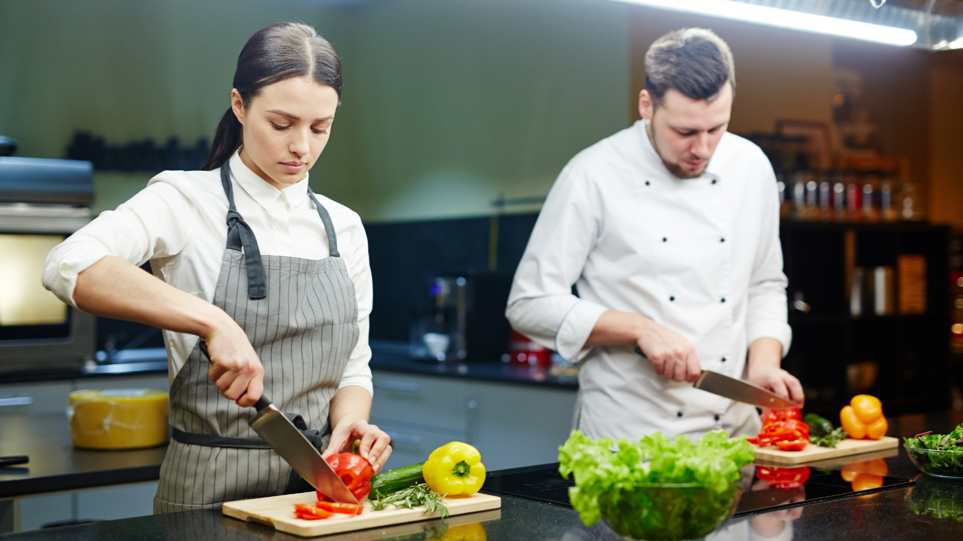 Two people slicing food in a professional kitchen. Hotel and kitchen jobs are expected to grow this year.