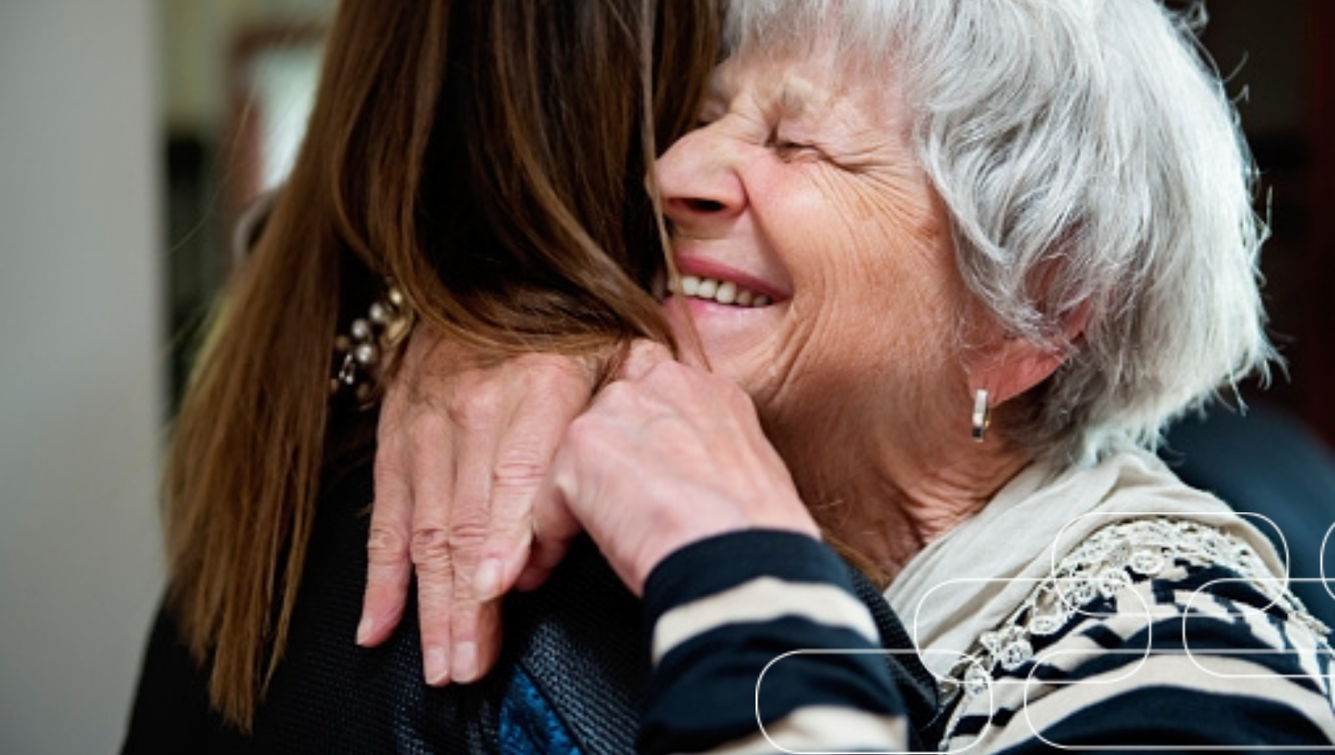 An female older adult with silver hair happily embracing a woman with long brown hair