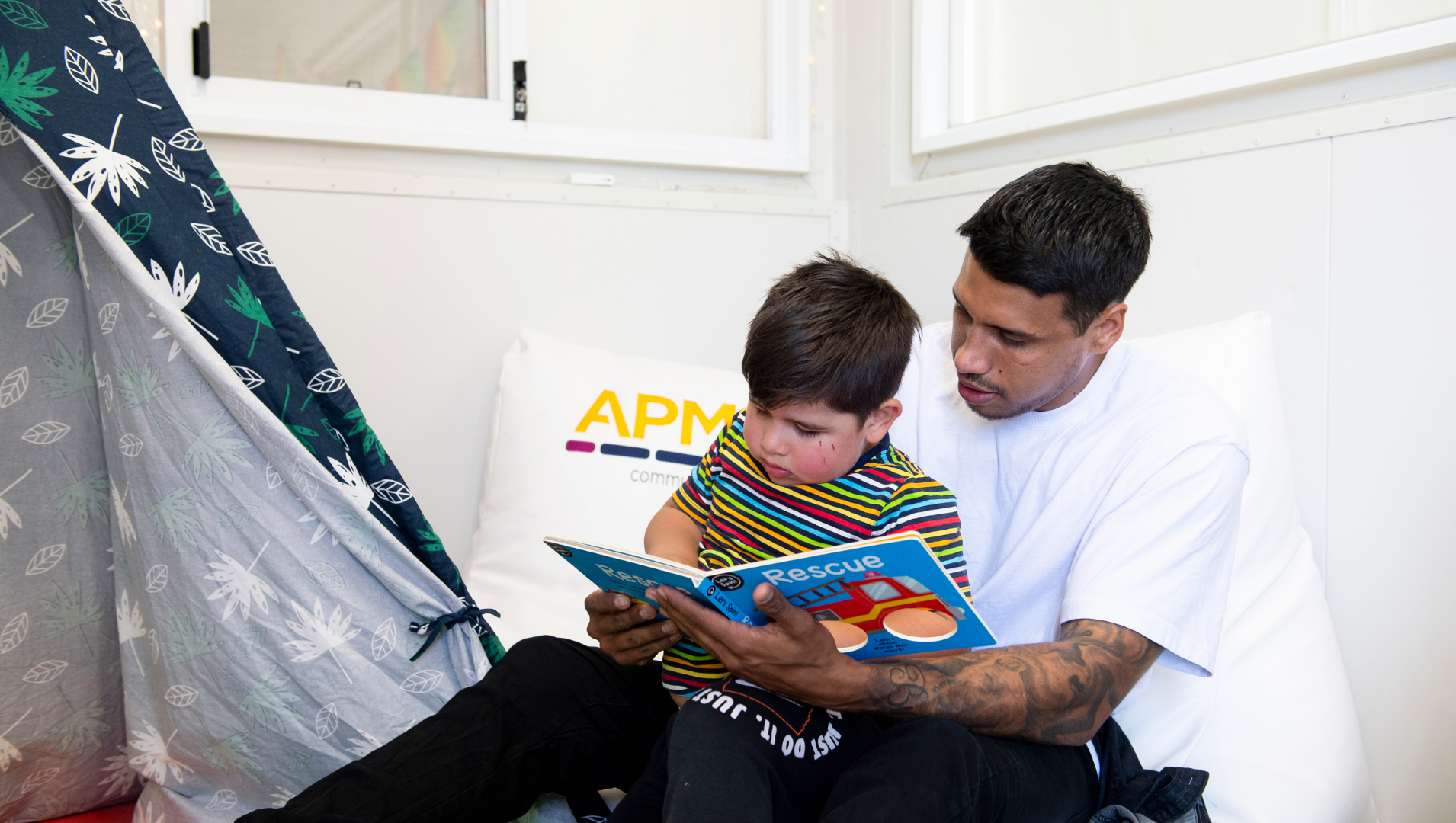 Tim Kelly sitting in the chill out zone with his son, reading a book