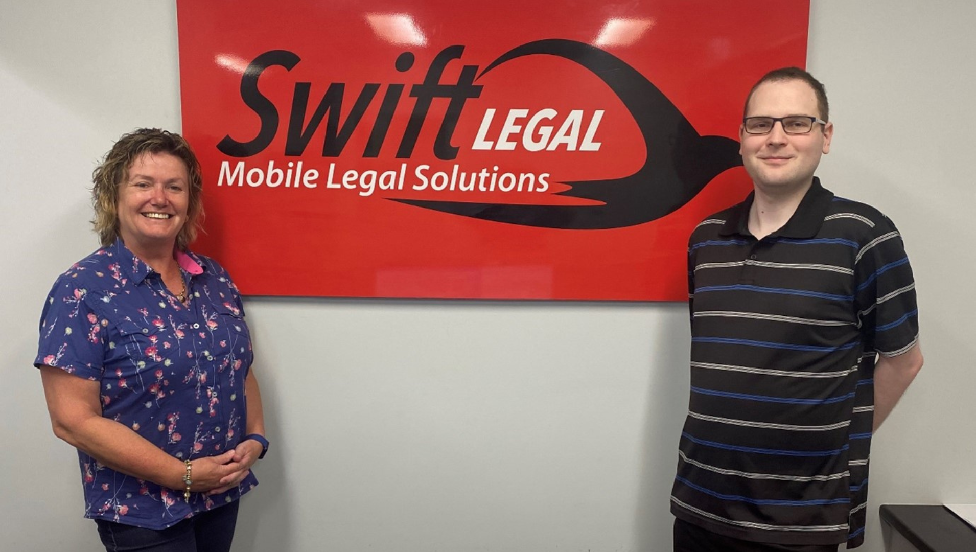 Chris standing next to his employer Judica, standing in front of a large red Swift Legal sign