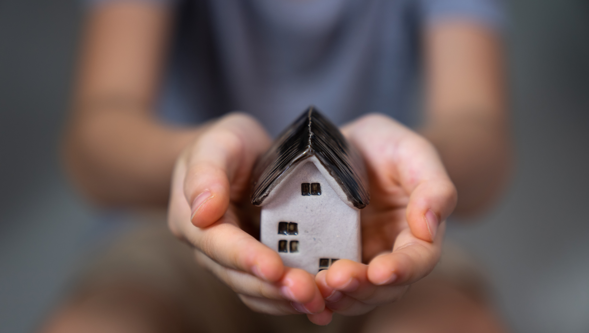 A child's hands cupping a small ceramic house, the background of the photo is blurred
