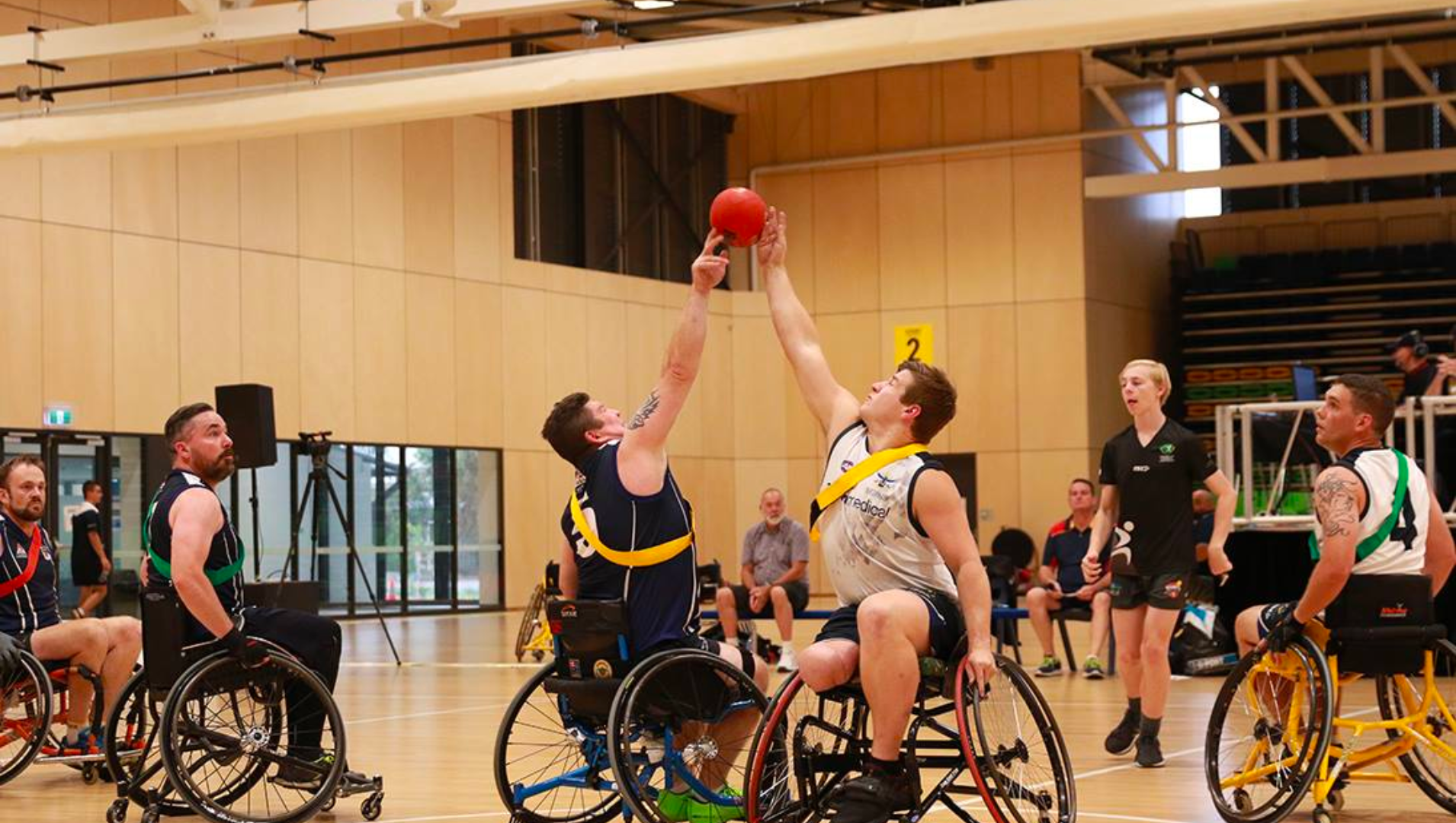 Action shot from a wheelchair AFL game showing two players going into tap a ball with their arms extended