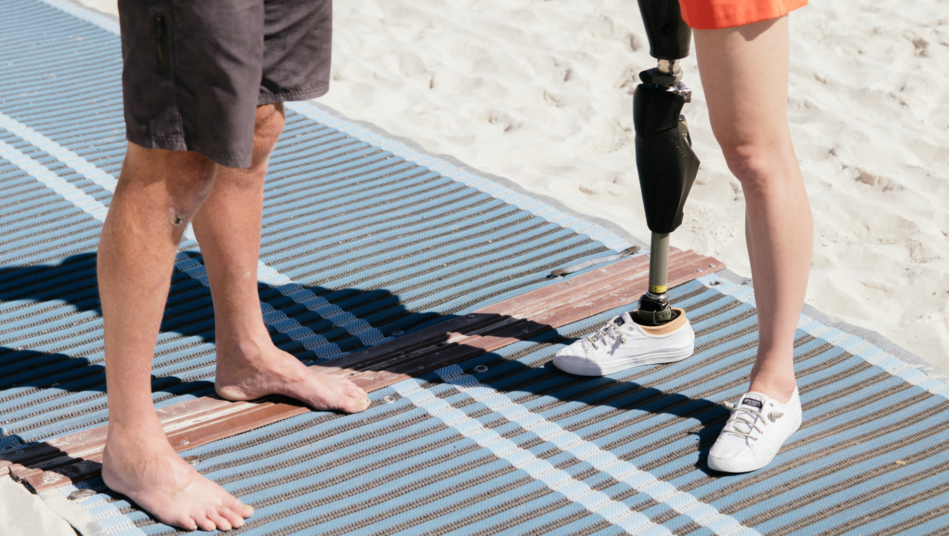 Two pairs of legs on a mobi mat surrounded by beach sand