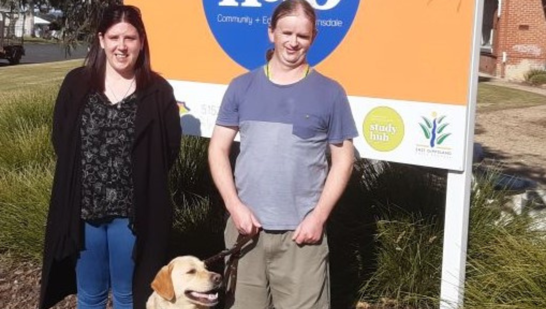 Ben standing in front of a community centre sign, with his golden Labrador guide dog