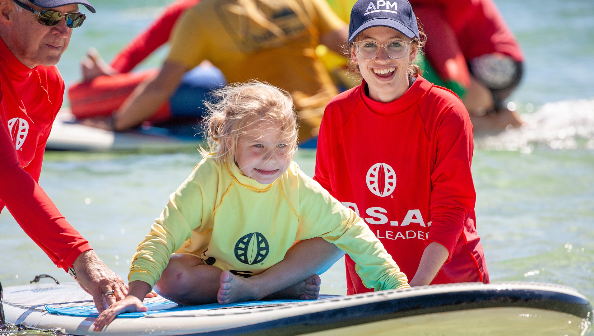 Two members of APM Communities assist a young child to float along on a SUP board