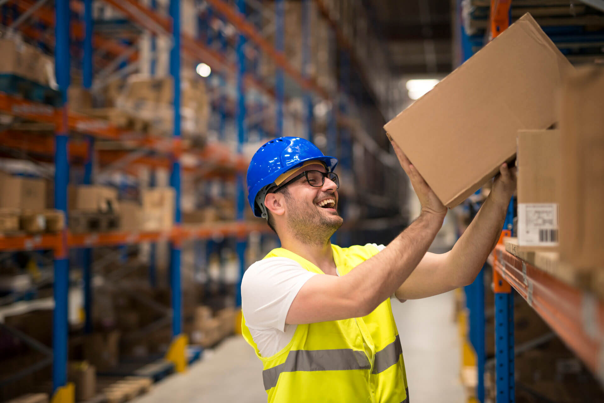 Worker stacking shelves in a warehouse safely and pain free with a smile on his face