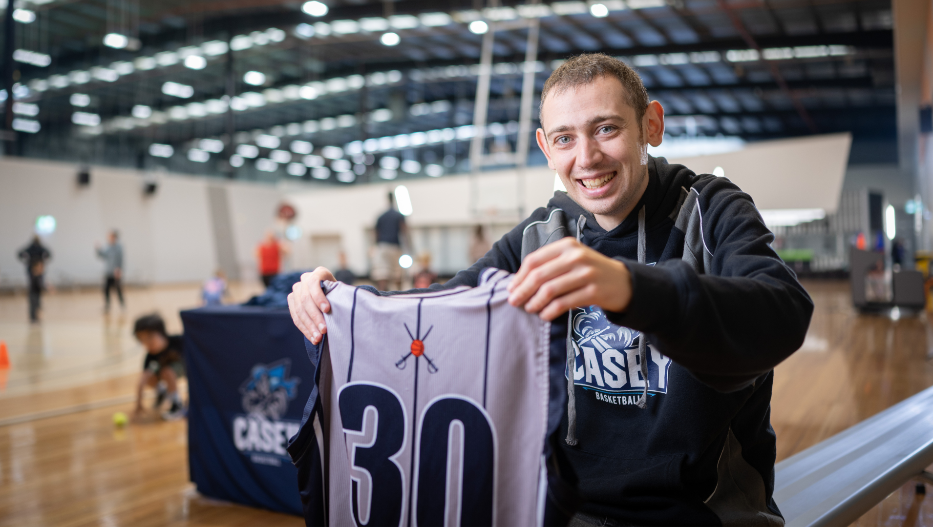 Aiden is pictured at the basketball stadium holding a jersey and smiling